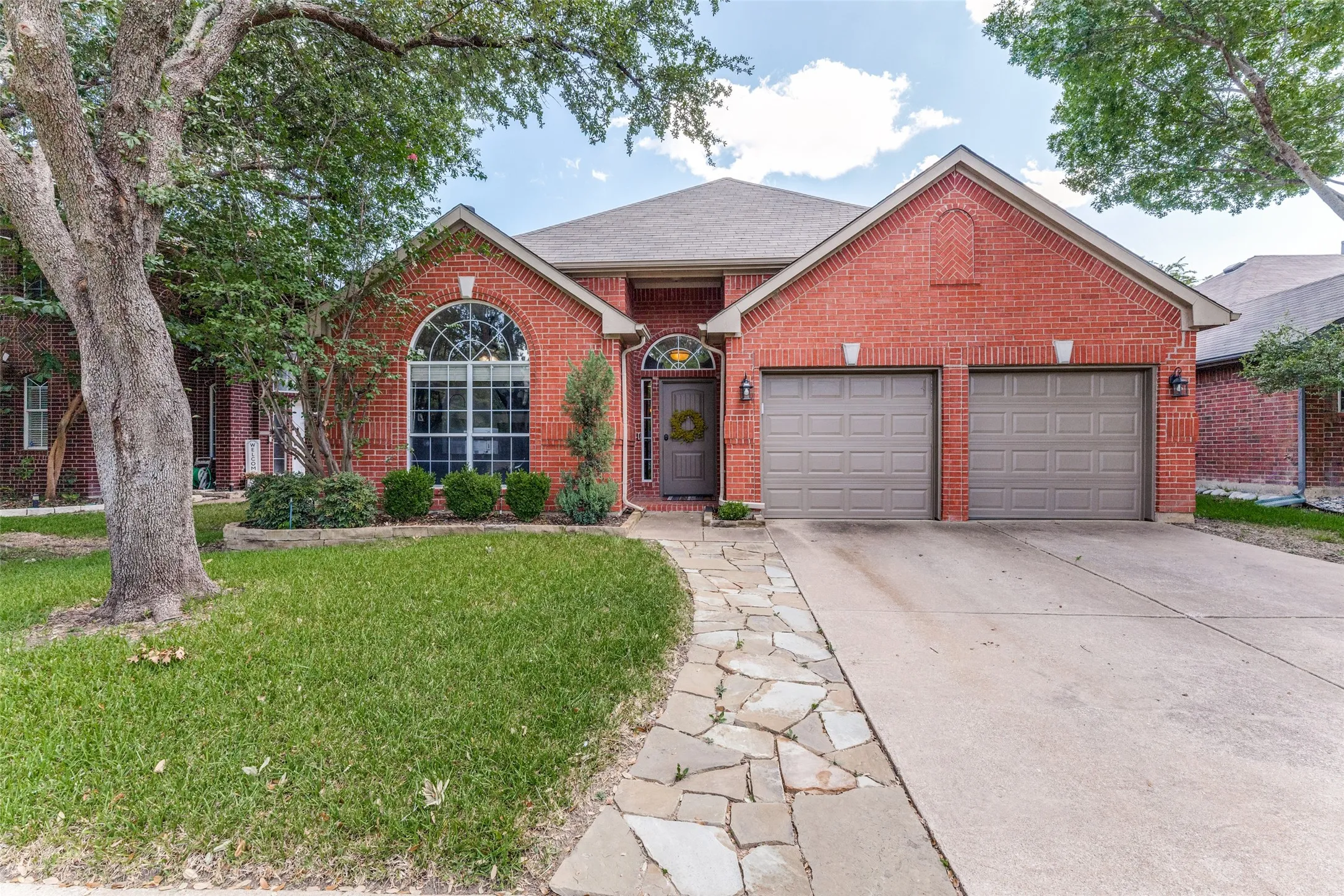 Red brick exterior featuring a multi-gabled roofline, an arched entry, and a two-car garage