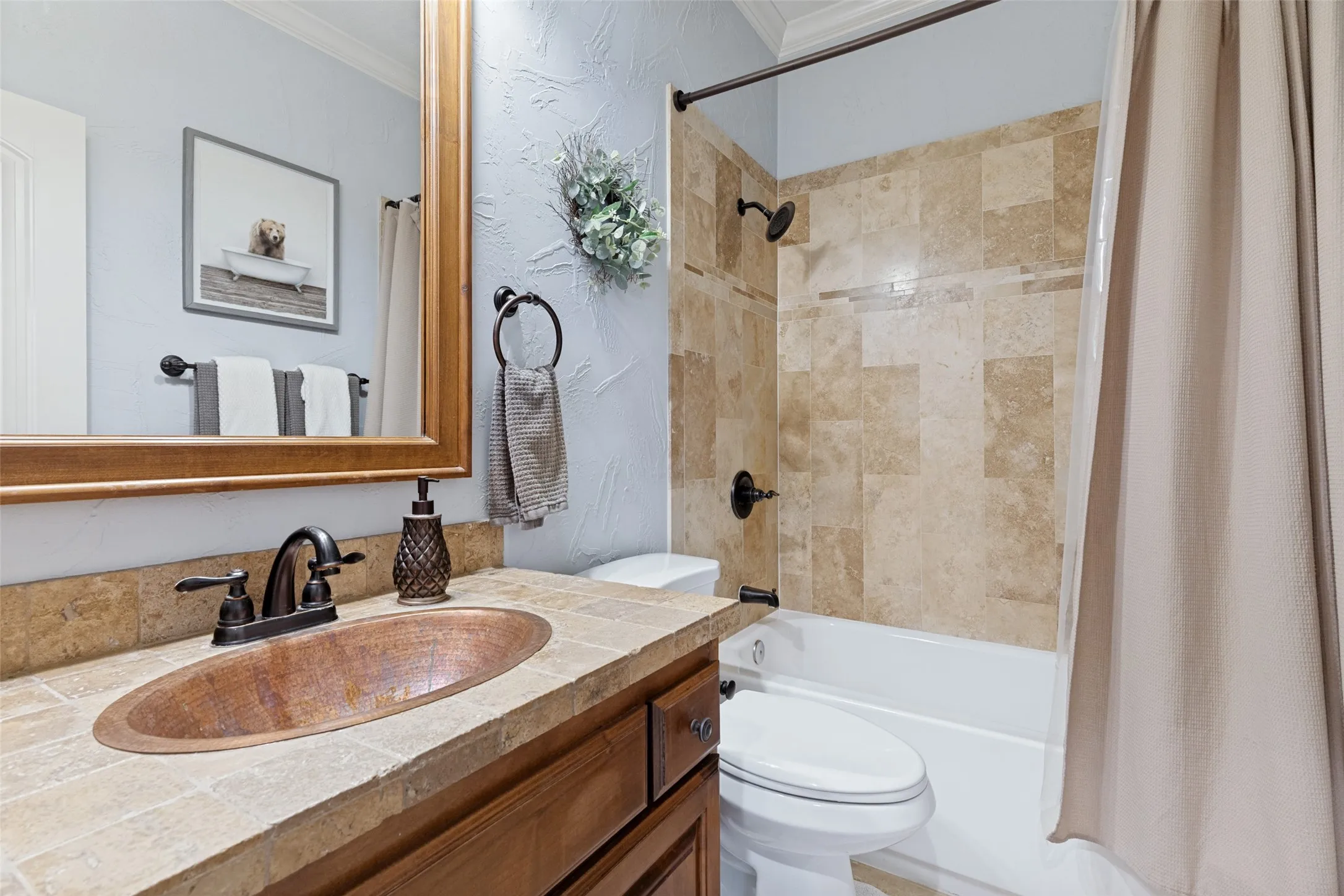 Bathroom featuring a copper vessel sink, dark bronze fixtures, a tiled vanity countertop, a mirror with a wood frame, and a tiled shower surround