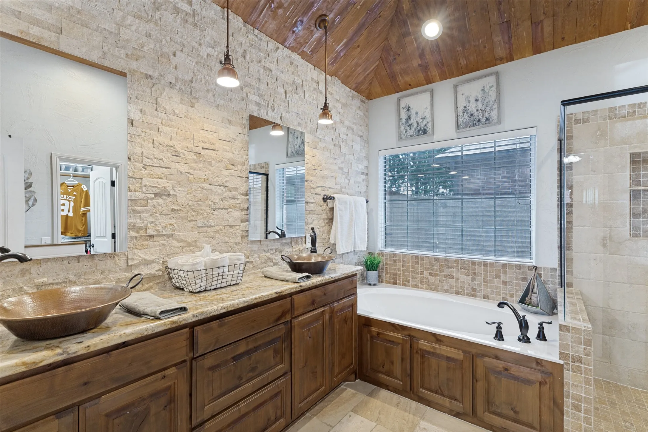 Bathroom featuring a vaulted wood-plank ceiling, natural stone accent wall, dual vessel sinks, and a built-in soaking tub with mosaic tile surround and separate shower