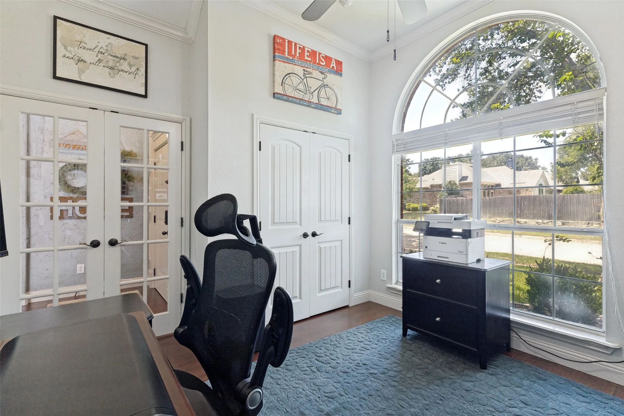 Room featuring a large arched window with blinds, wood-finish flooring, white paneled doors, and a ceiling fan