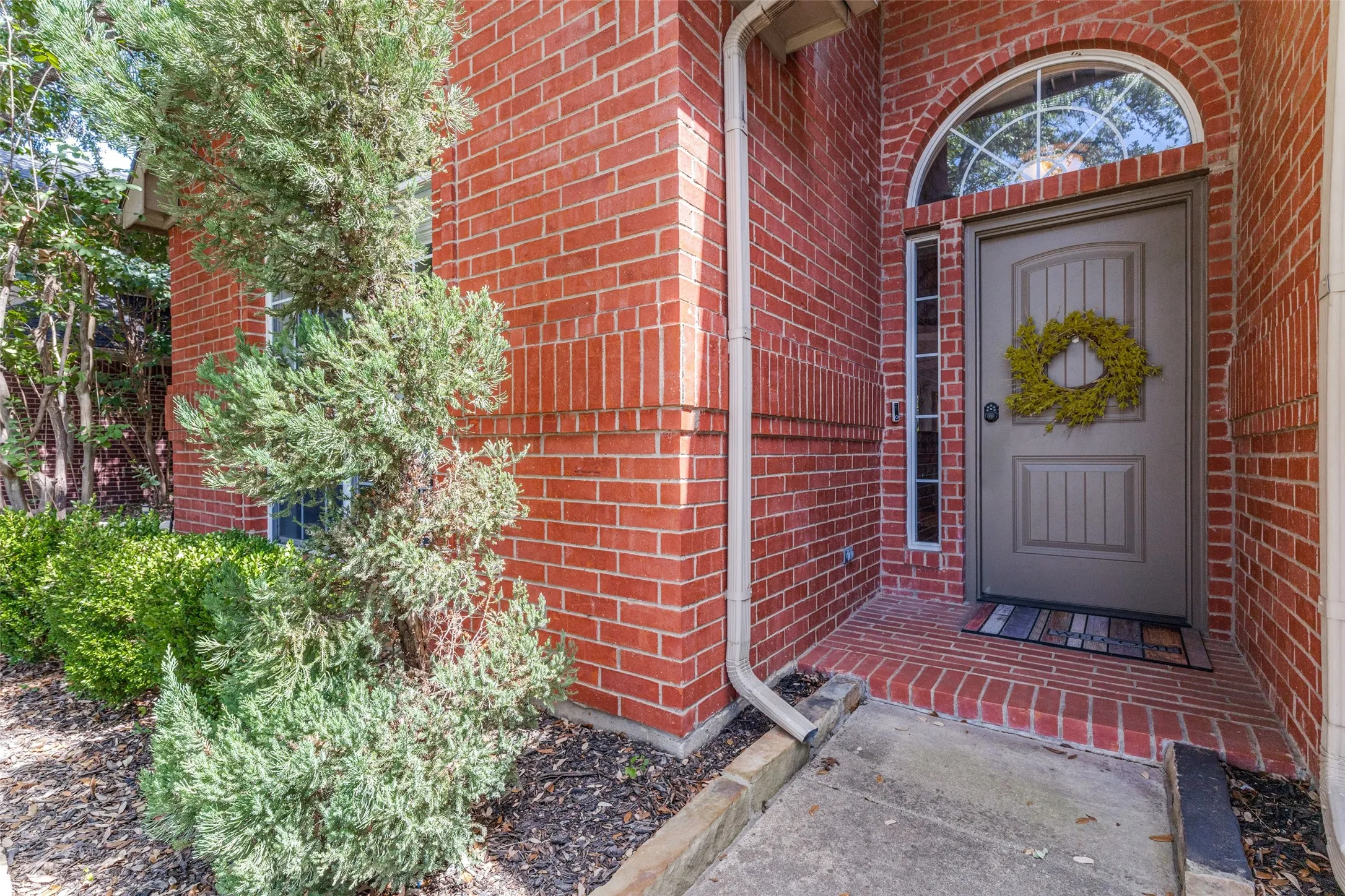 Red brick exterior featuring an arched transom window, a rectangular sidelight, and a gray paneled entry door