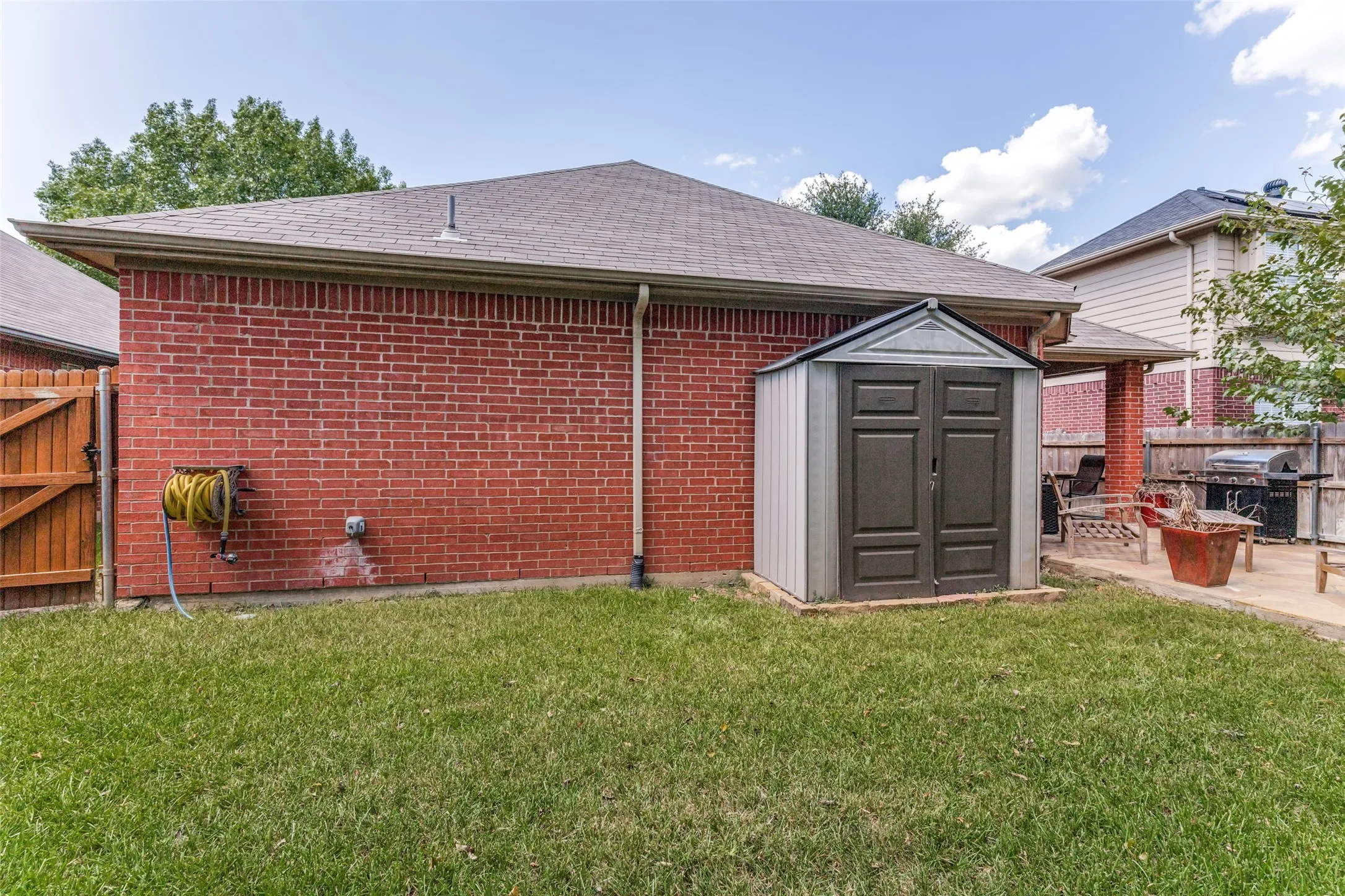 Manicured lawn with brick exterior, a utility shed, and a covered patio area