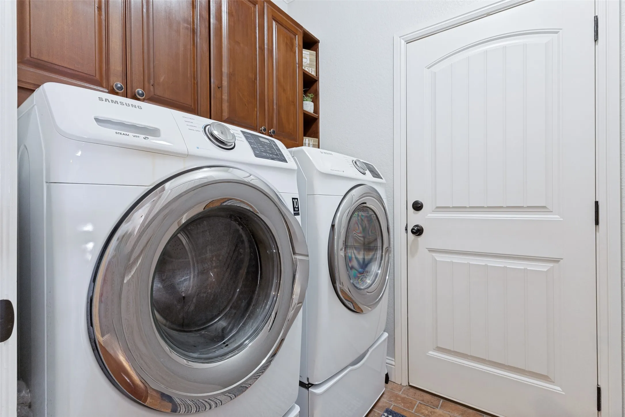 Dedicated laundry area featuring dual front-loading appliances, rich wood cabinetry, and a paneled white door