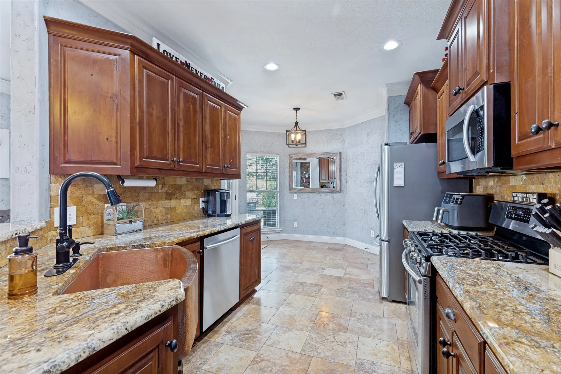 Kitchen featuring rich wood cabinetry, granite countertops, a copper farmhouse sink with a matte black faucet, and stainless steel appliances
