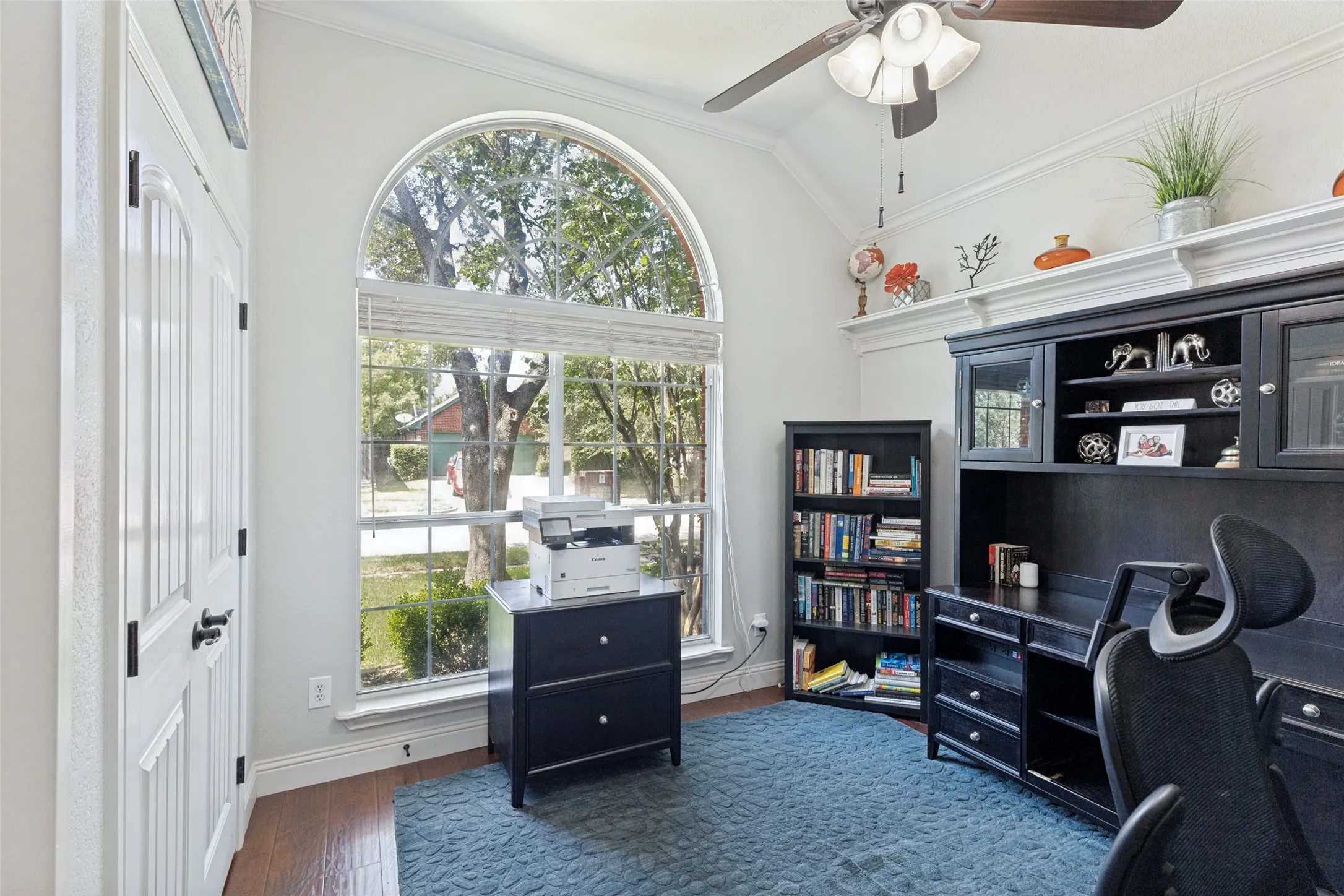 Room featuring an arched window, wood-finish flooring, a ceiling fan with integrated lighting, built-in shelving, and white paneled doors with dark hardware