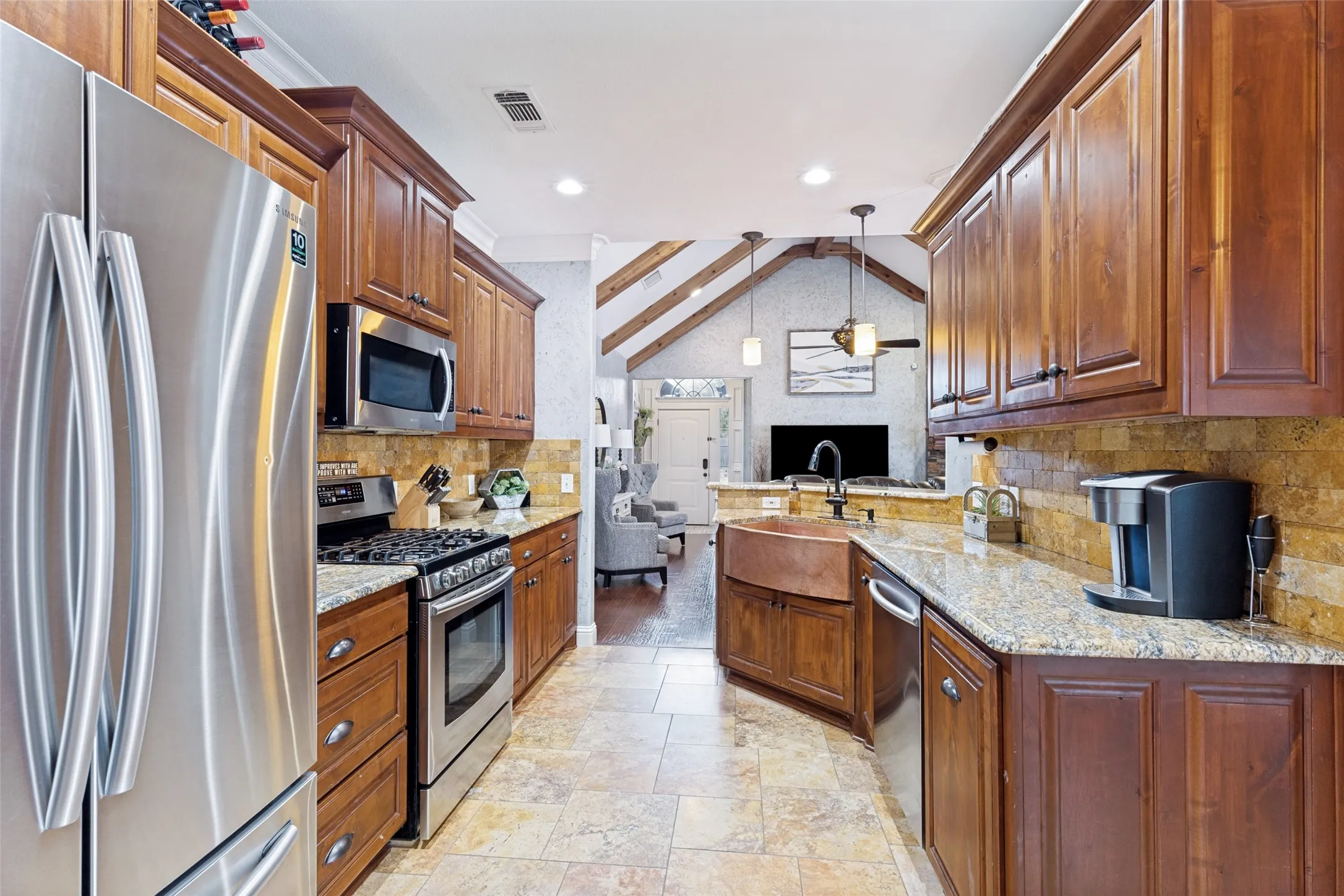 Open kitchen featuring stainless steel appliances, wood cabinetry, granite countertops, and stone tile flooring