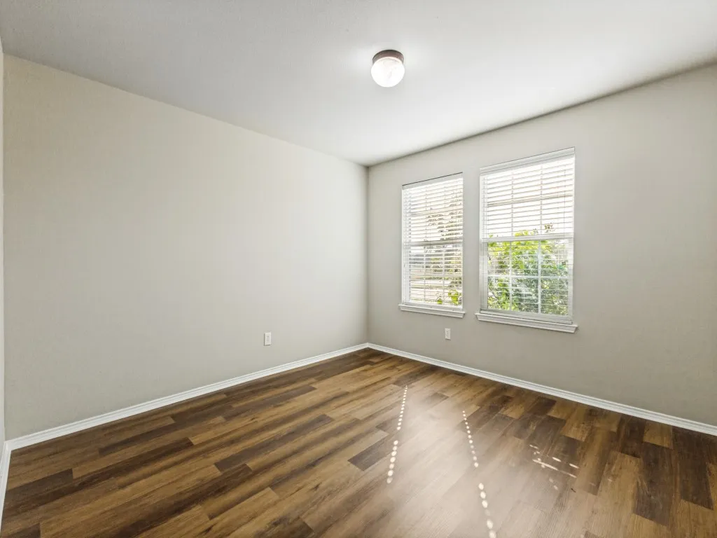 Wood-finish flooring, two windows with blinds, light gray wall paint, and a ceiling-mounted light fixture