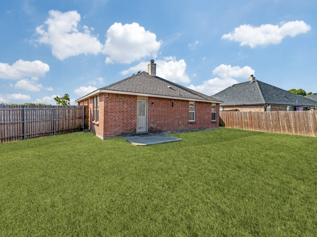 Expansive backyard with a manicured lawn, brick exterior, wood fence, and a concrete patio