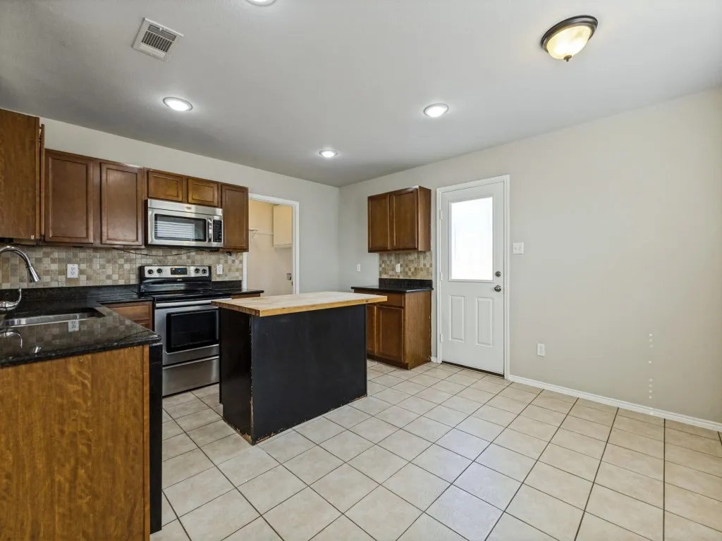 Kitchen featuring a center island, tile flooring, wood cabinetry, stainless steel appliances, and a tiled backsplash