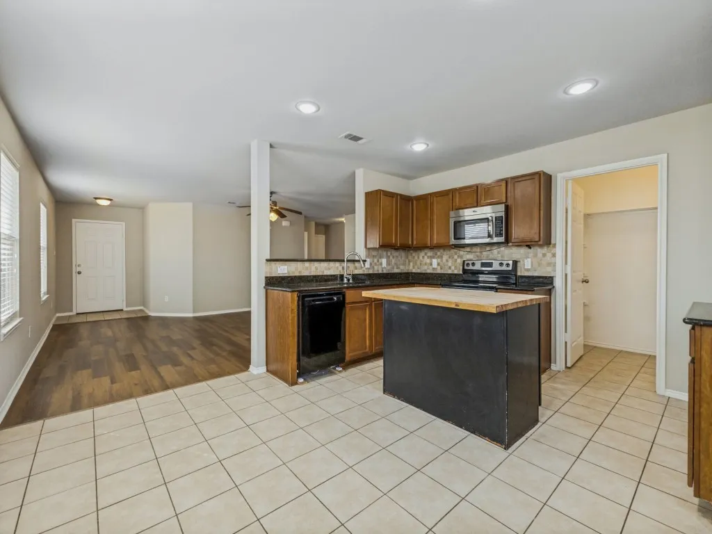 Kitchen featuring tile flooring, wooden cabinetry, dark countertops, and a central island with a wood-finish top