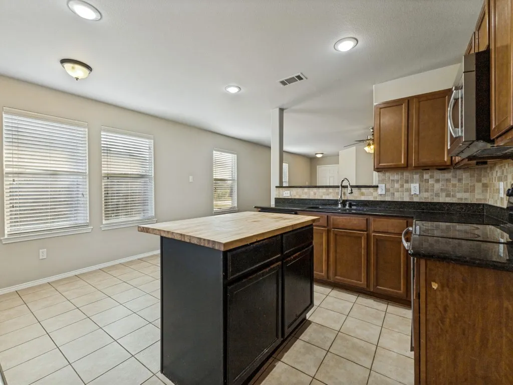 Kitchen featuring a central island with a wood-finish countertop, tile flooring, brown cabinetry, black countertops, and a mosaic tile backsplash