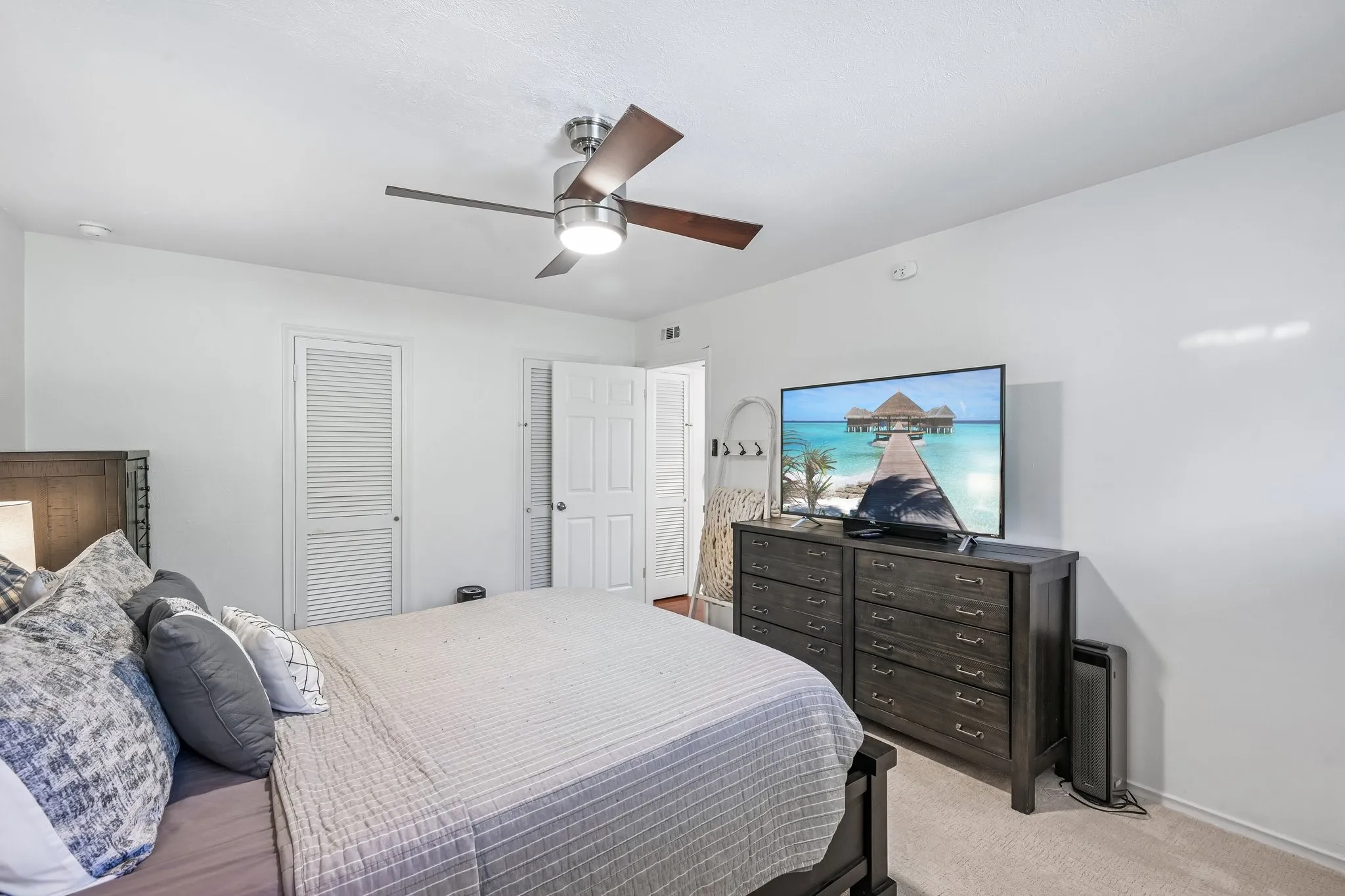 Bedroom featuring light-colored carpeting, a ceiling fan with wood-finish blades, and white painted walls