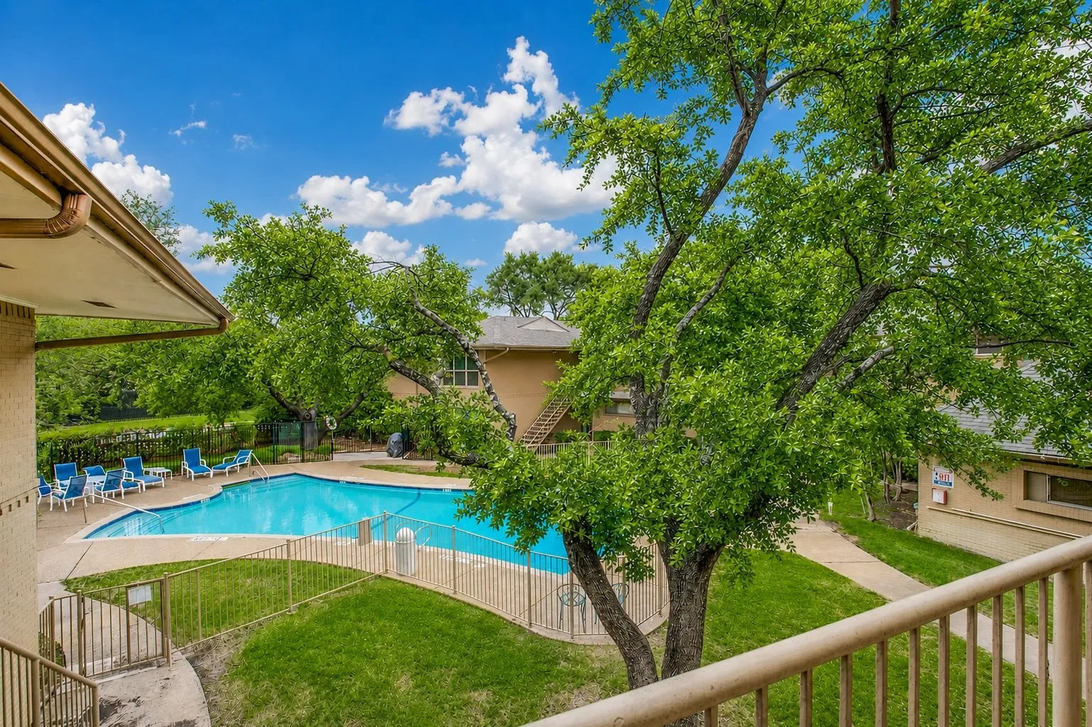 Outdoor swimming pool with integrated steps, surrounded by a concrete deck and metal fencing