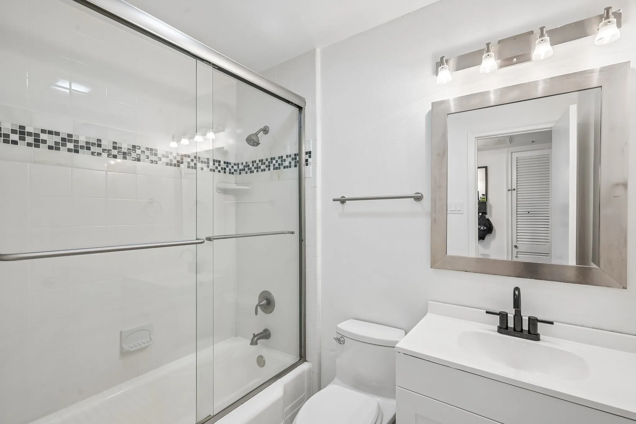Bathroom with a white tile tub/shower combination, mosaic tile accent band, and clear glass sliding doors