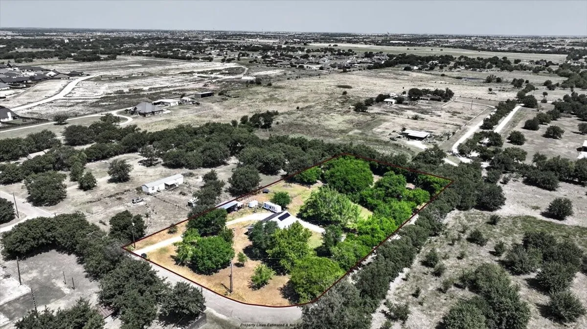 Aerial view with estimated property lines, mature trees, and surrounding land
