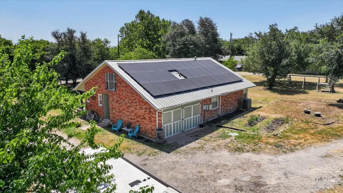 Rear exterior with solar panels, metal roof, and gravel drive