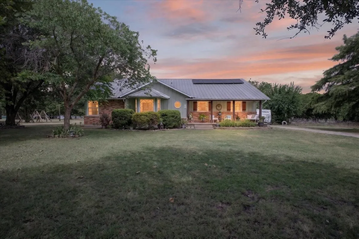 Twilight front exterior with metal roof, solar panels, and mature tree setting