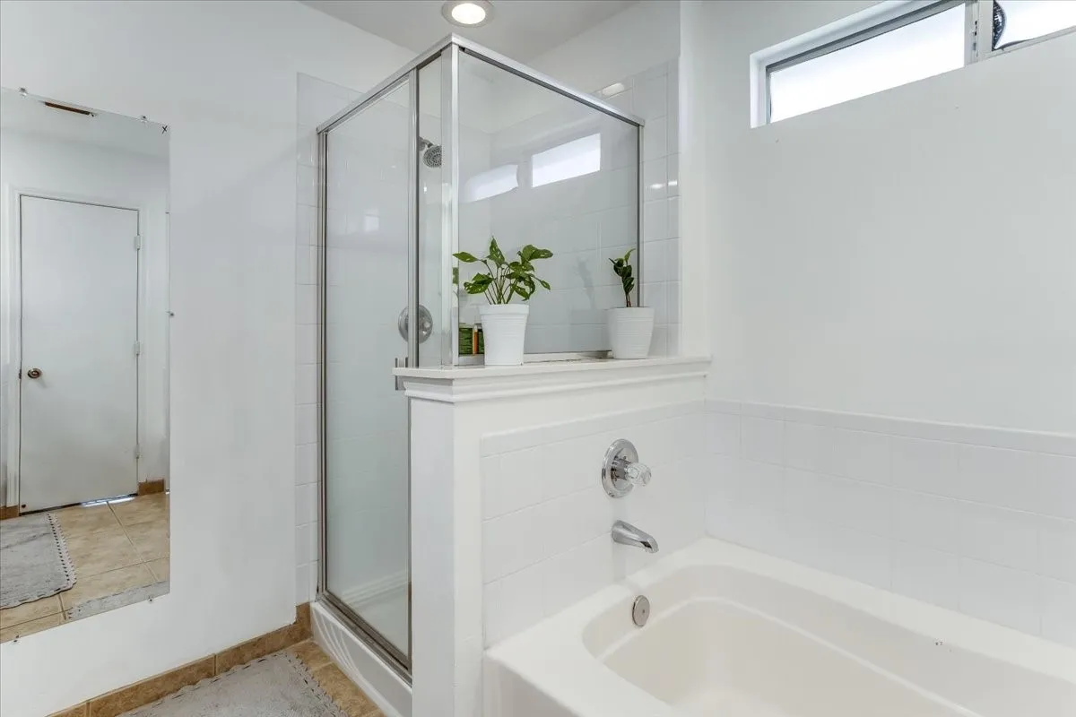 Bathroom featuring a glass-enclosed shower, a built-in bathtub with chrome fixtures, and a high horizontal window