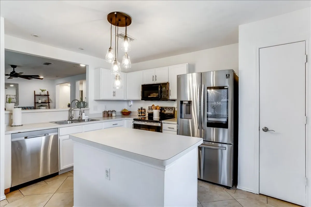 Contemporary kitchen featuring stainless steel appliances, white cabinetry, a central island, and a decorative multi-bulb pendant light fixture