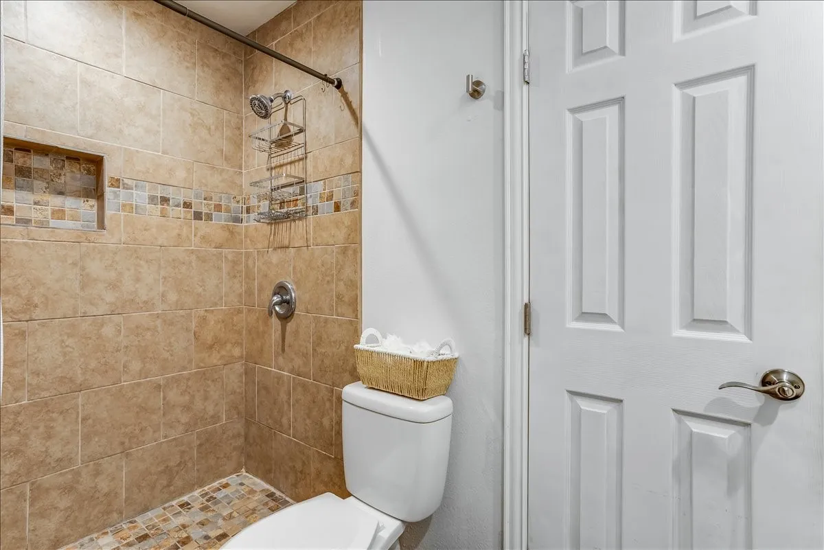 Shower with neutral-toned wall tiles, decorative accent tile band, and a mosaic tile shower floor