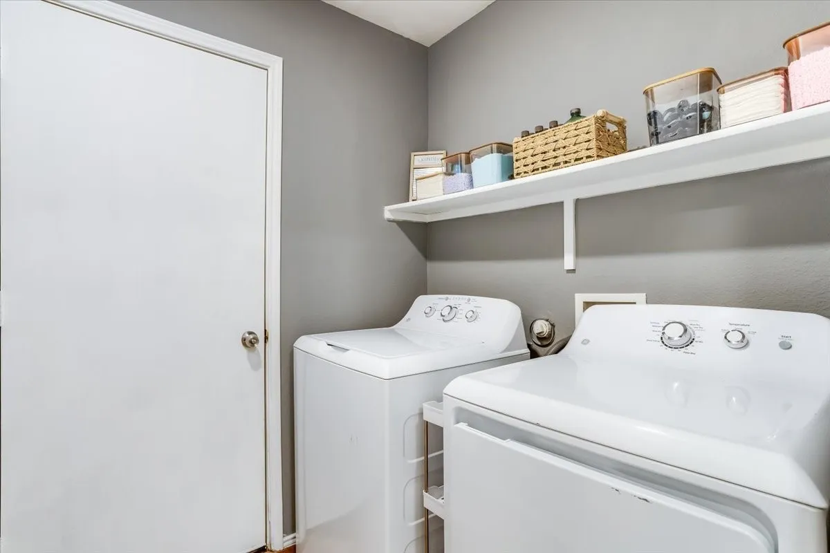 Dedicated utility area featuring a washer and dryer, painted walls, and an overhead shelf for storage