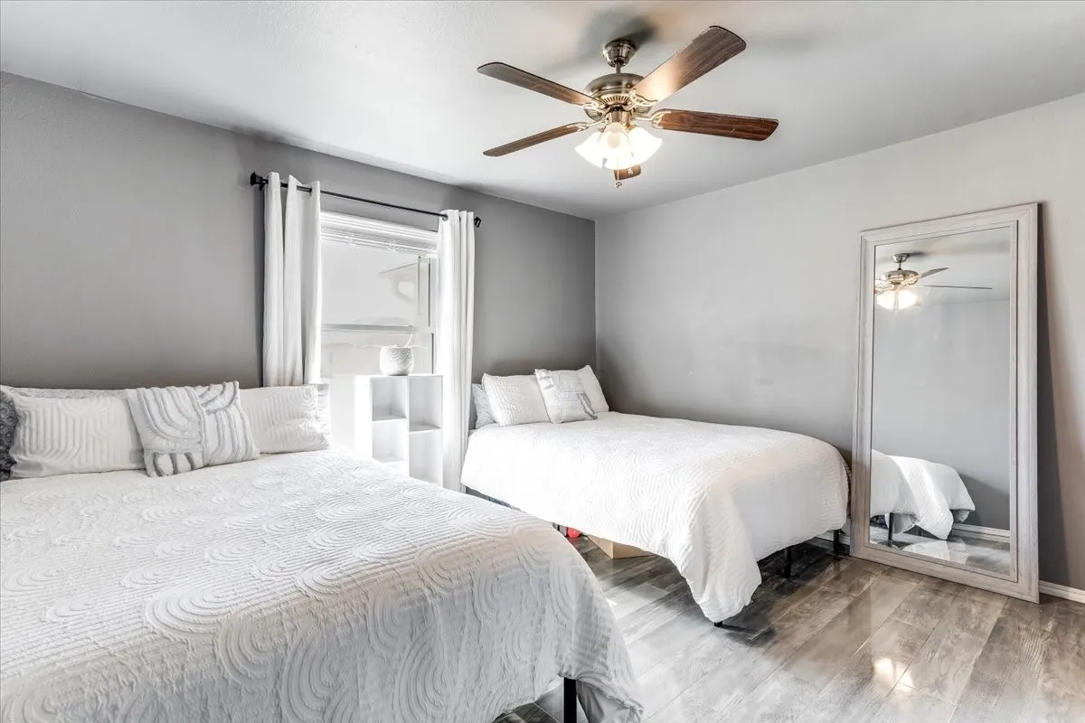Room featuring wood-finish flooring, a ceiling fan with integrated lighting, and a single window with white drapery