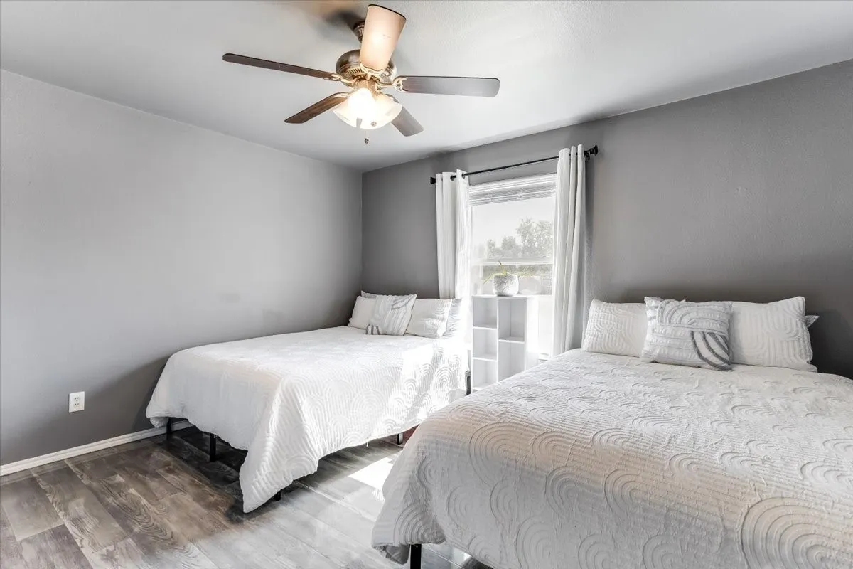 Bedroom featuring wood-finish flooring, a ceiling fan with integrated lighting, and a window with white curtains