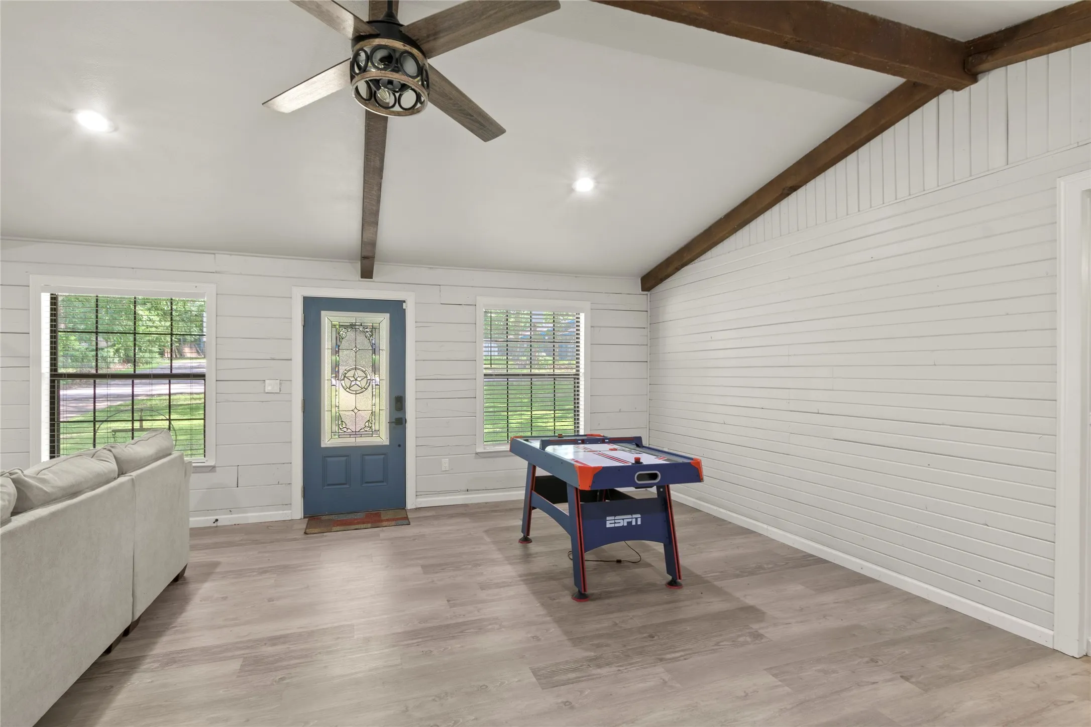 Spacious room featuring wood-finish flooring, white shiplap walls, and exposed ceiling beams