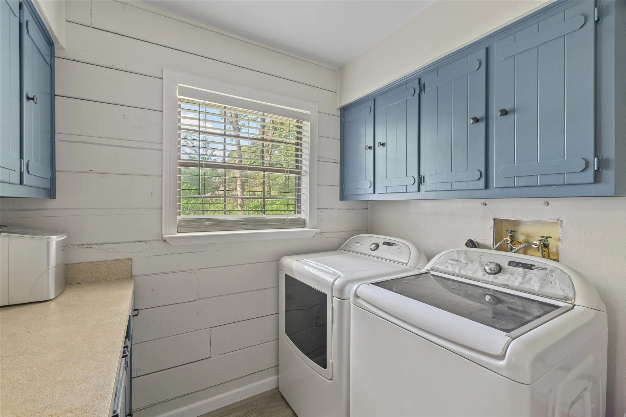 Utility room featuring wood-plank accent wall, built-in cabinetry with blue finish, window with natural light, and countertop space
