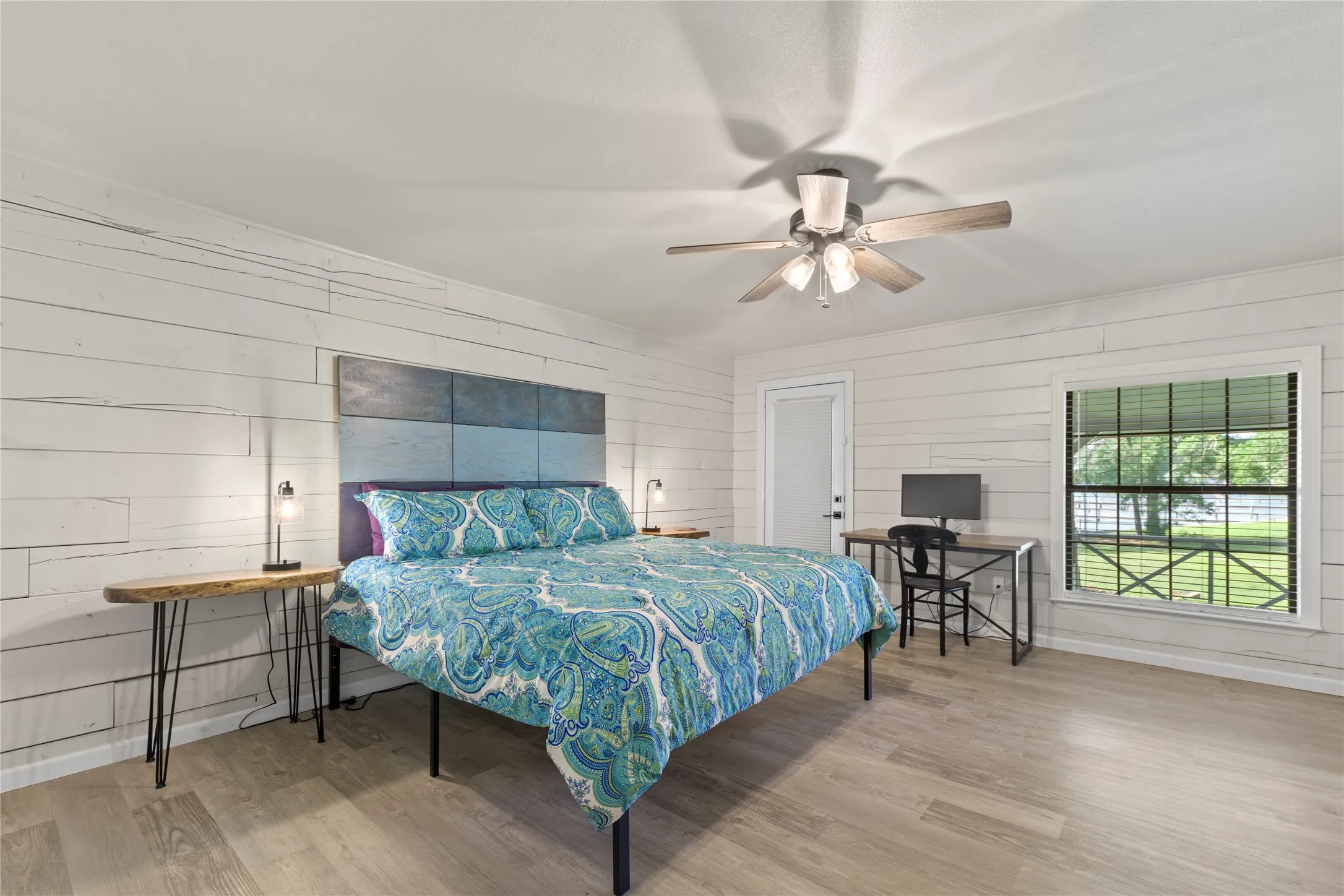 Bedroom featuring wood-finish flooring, white shiplap walls, a ceiling fan with light fixture, a window with blinds, and a white interior door