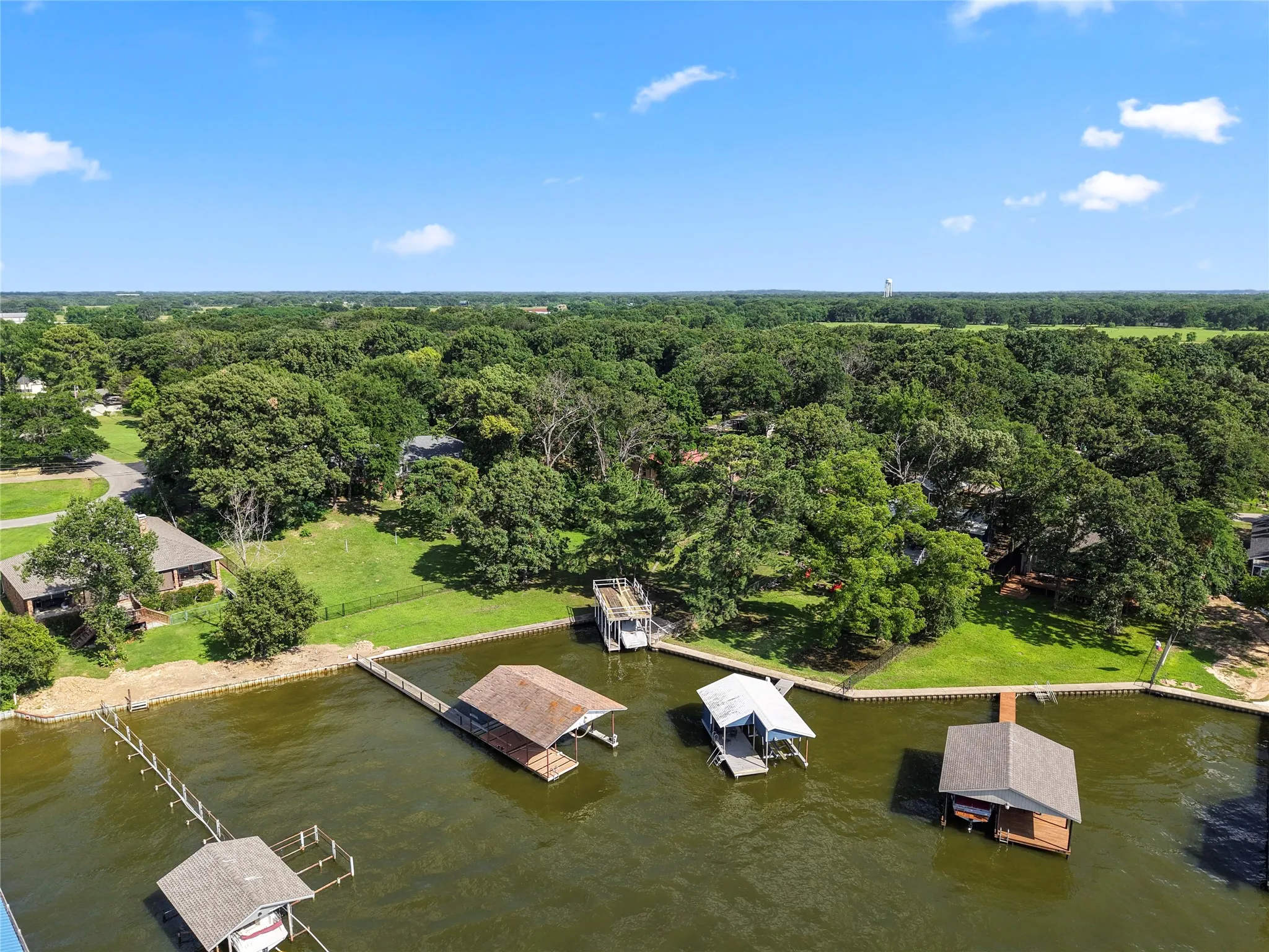 Waterfront property featuring multiple boat docks, mature trees, and a clear blue sky