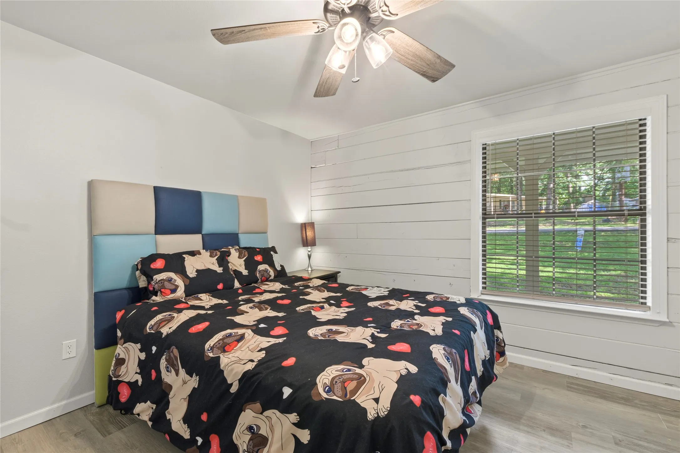 Bedroom featuring a shiplap accent wall, wood-finish flooring, and a ceiling fan with integrated lighting