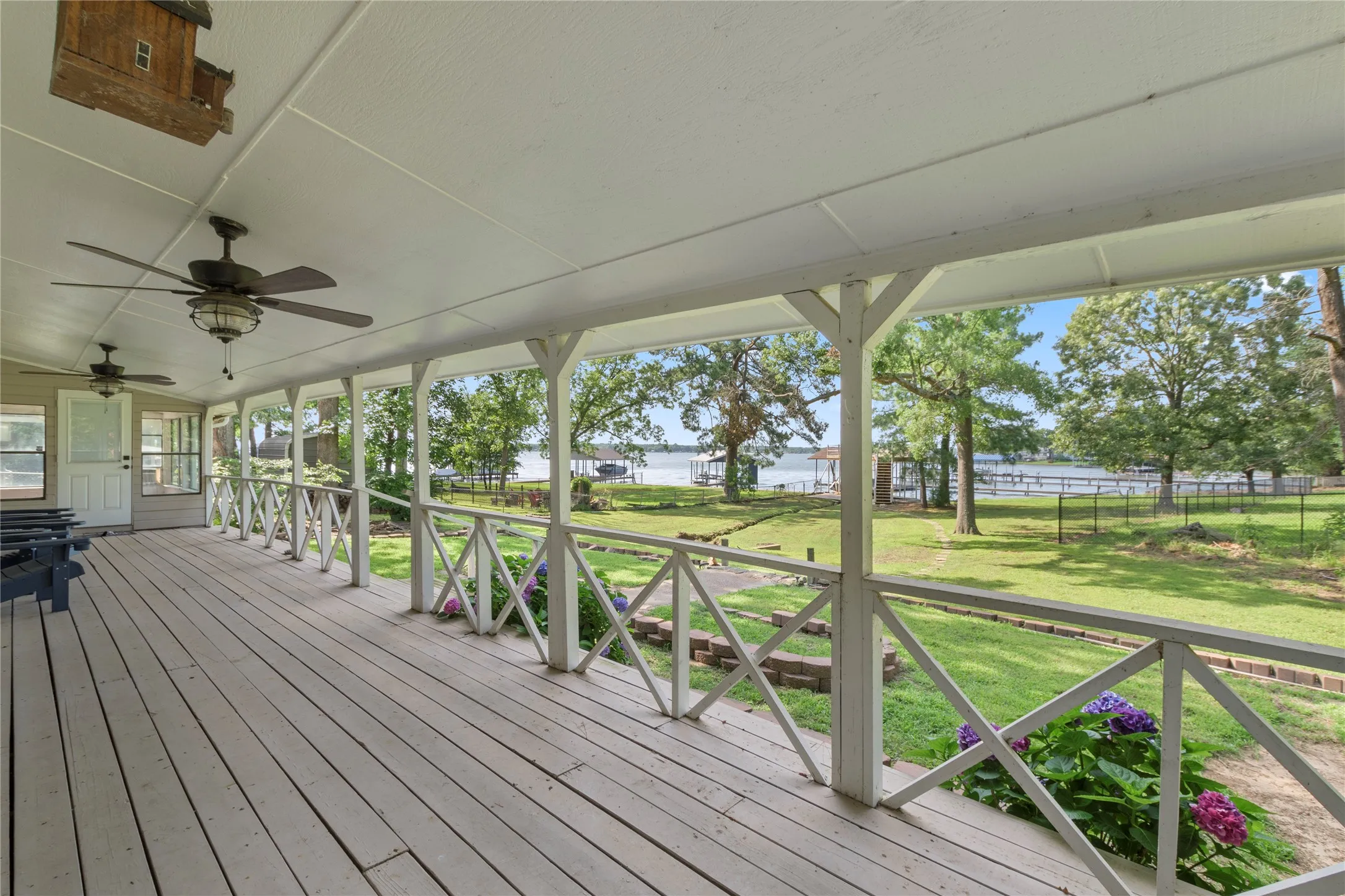 Expansive covered porch featuring wood-finish flooring, multiple ceiling fans, and decorative railing