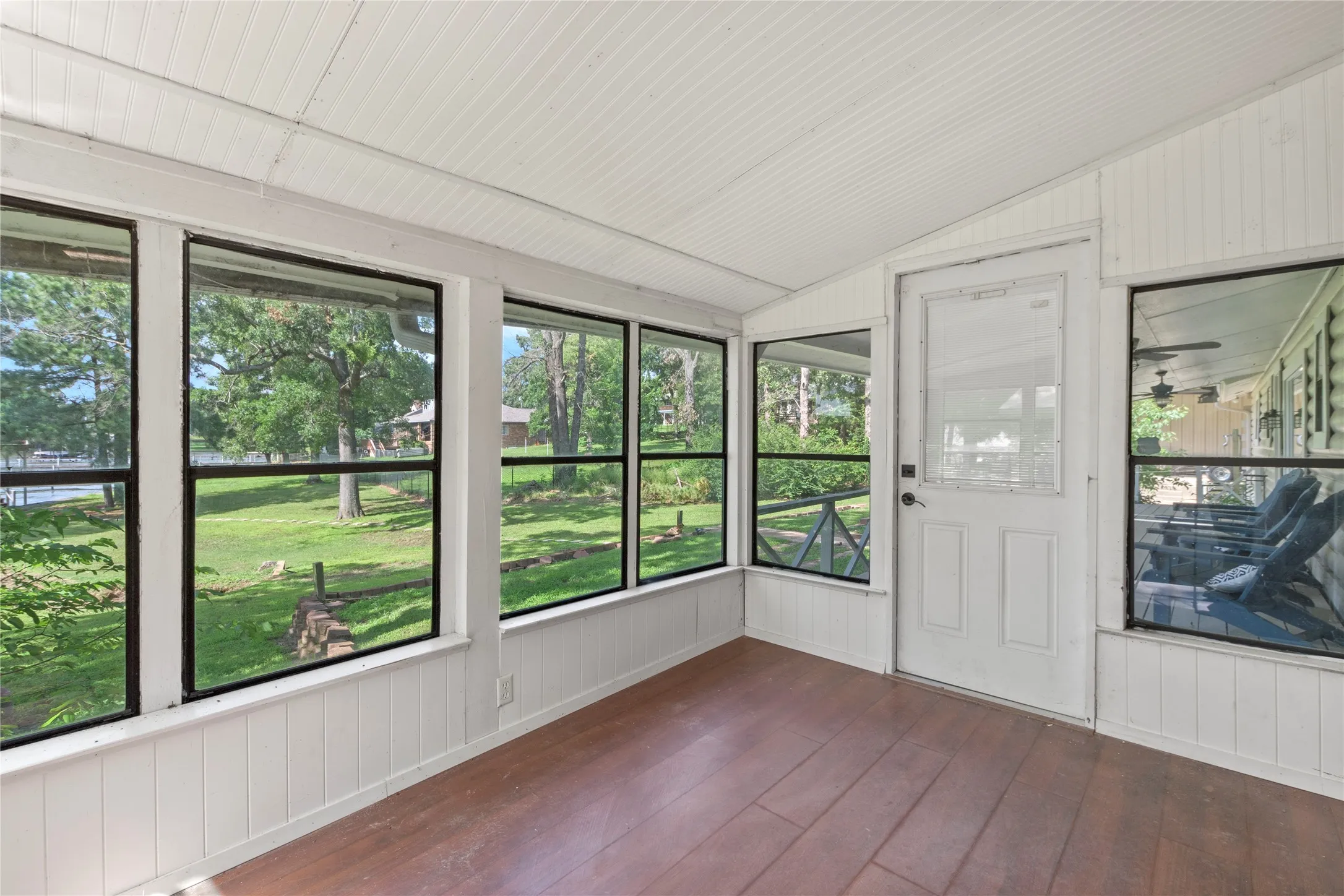 Enclosed sunroom featuring multiple large windows, wood-finish flooring, and white paneled walls and ceiling