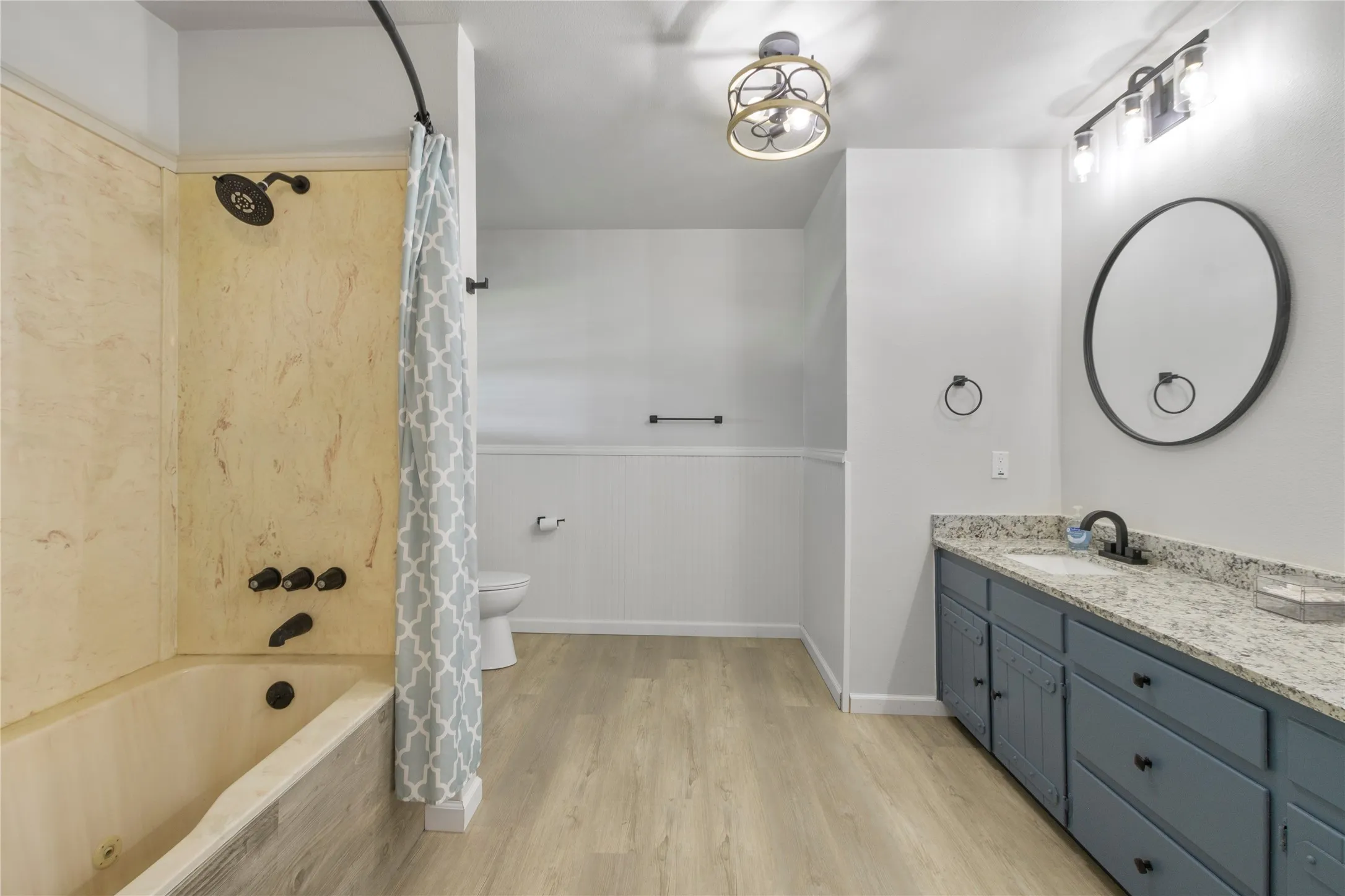 Spacious bathroom featuring a full tub and shower with stone-look surround and black fixtures