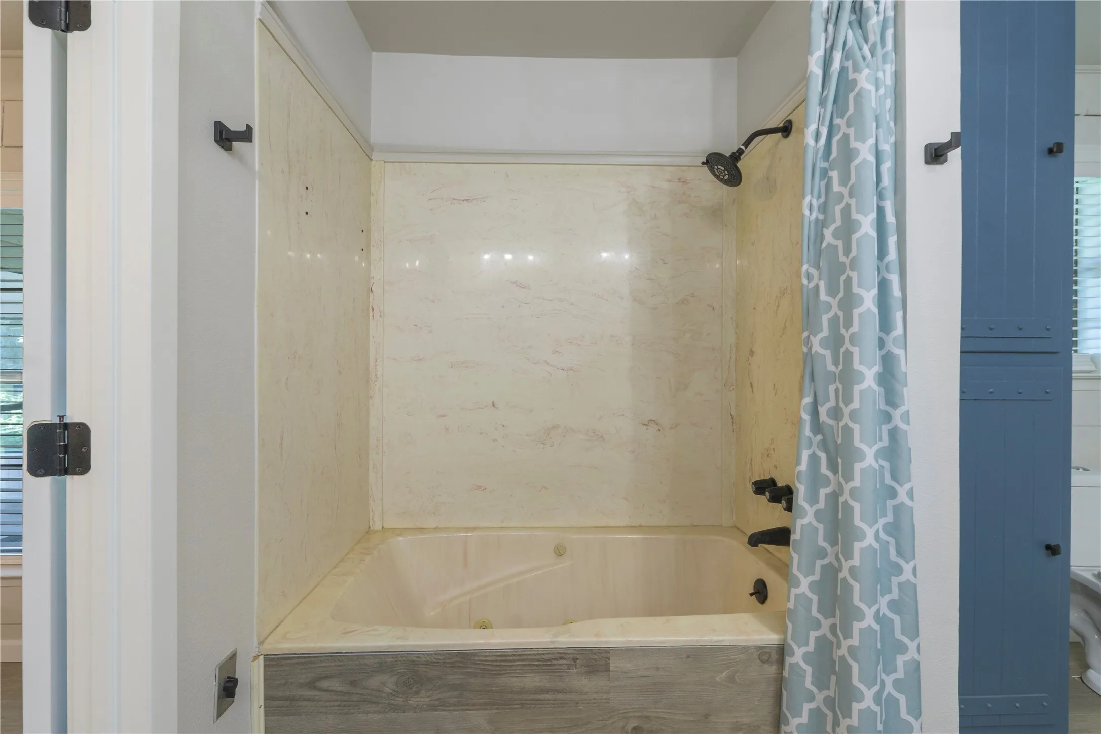 Tub/shower combination featuring a light-toned surround and dark-finish fixtures, complemented by a wood-finish tub skirt