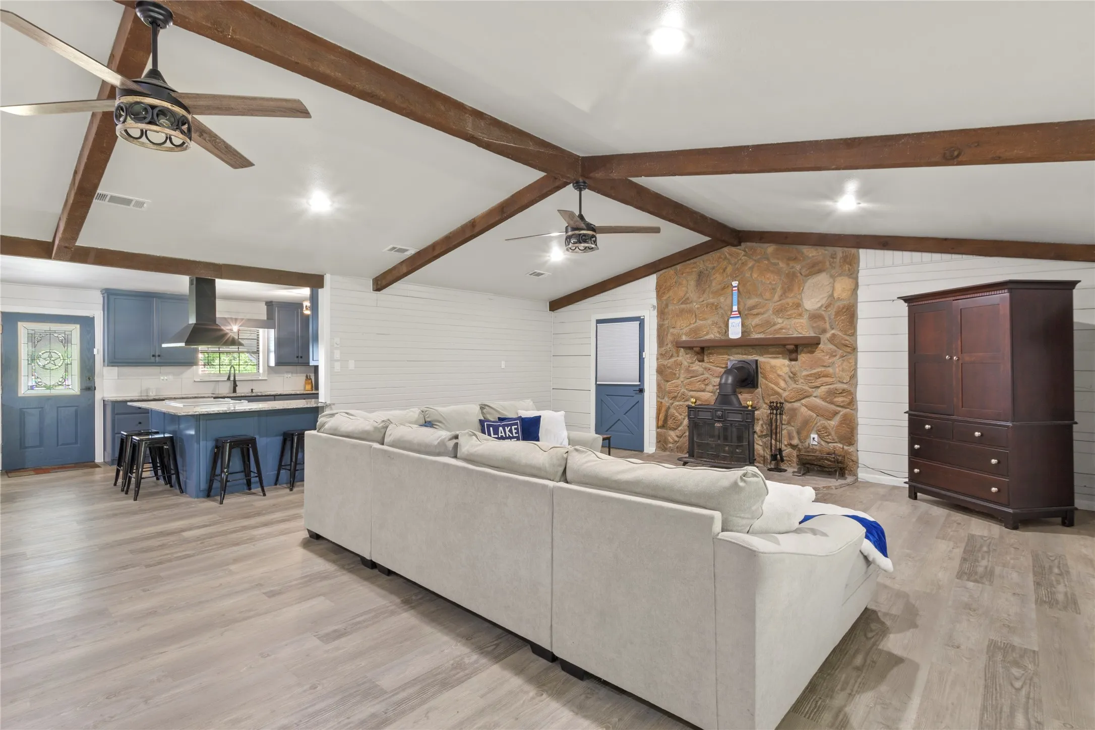 Spacious open-concept living area featuring a stone fireplace, exposed wood beams, and wood-finish flooring