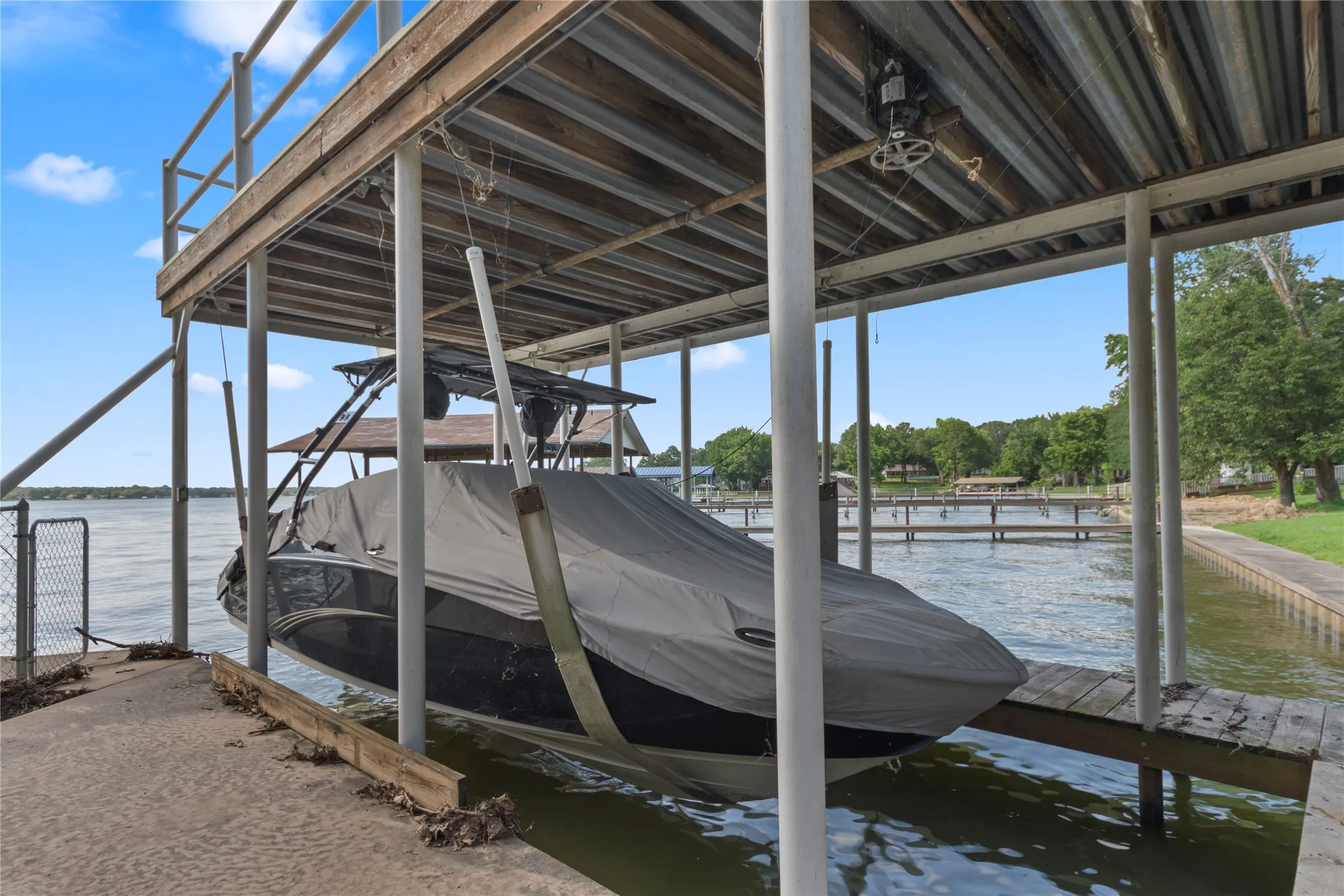 Covered boat dock featuring a boat lift, corrugated metal roof, and a wood decking upper level