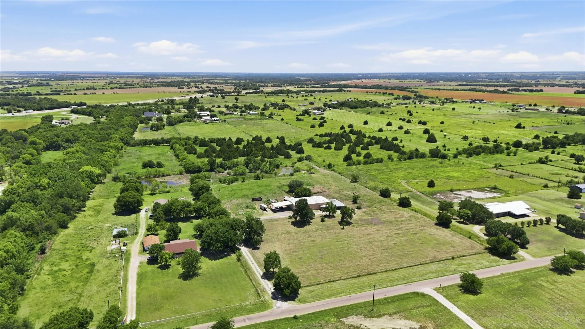 Expansive rural landscape featuring green pastures, scattered mature trees, and multiple residential structures
