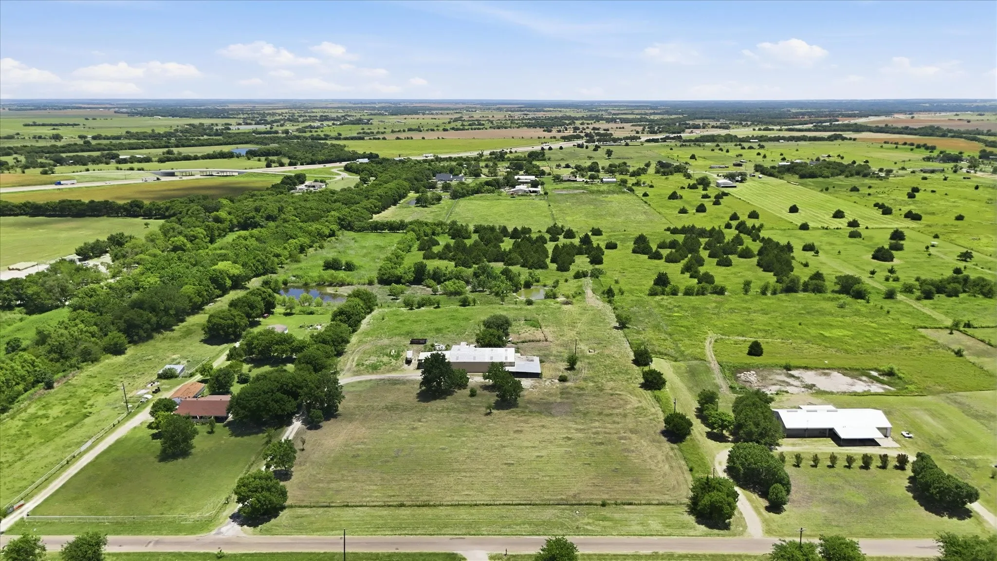 Expansive rural landscape featuring multiple structures, open fields, and numerous mature trees