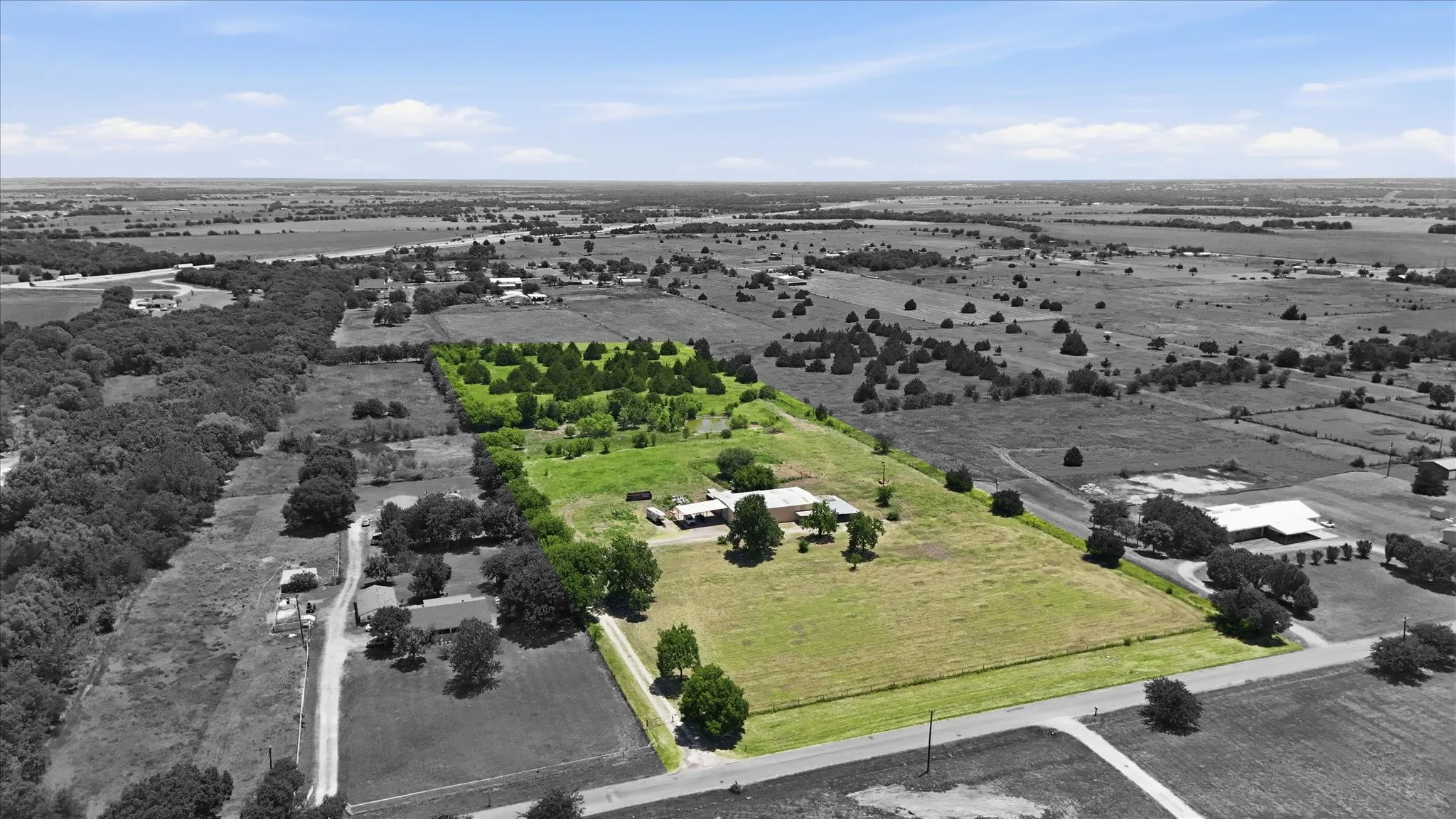 Expansive land parcel featuring open fields, scattered mature trees, and existing structures