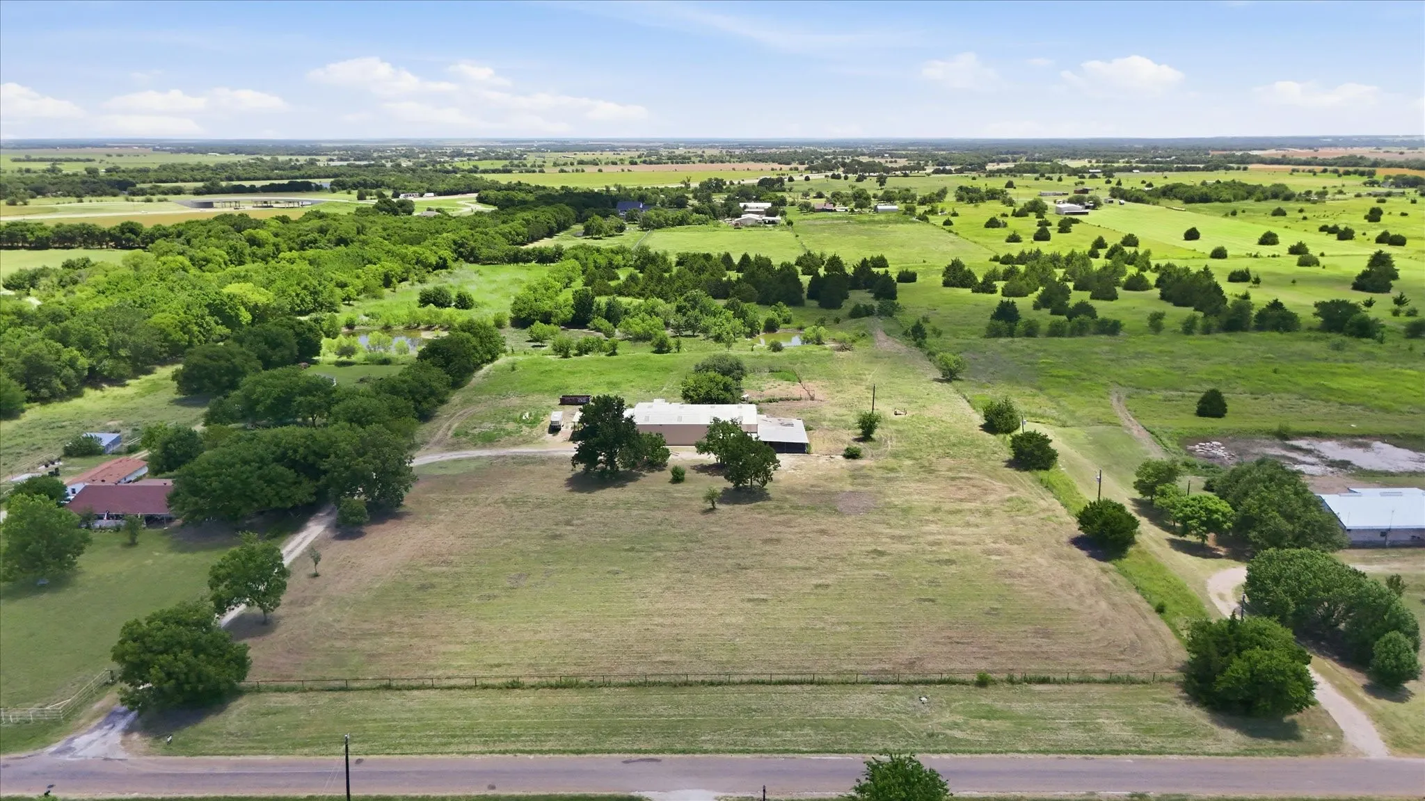 Expansive property featuring a central residence, surrounding open fields, mature trees, and a distant tree line