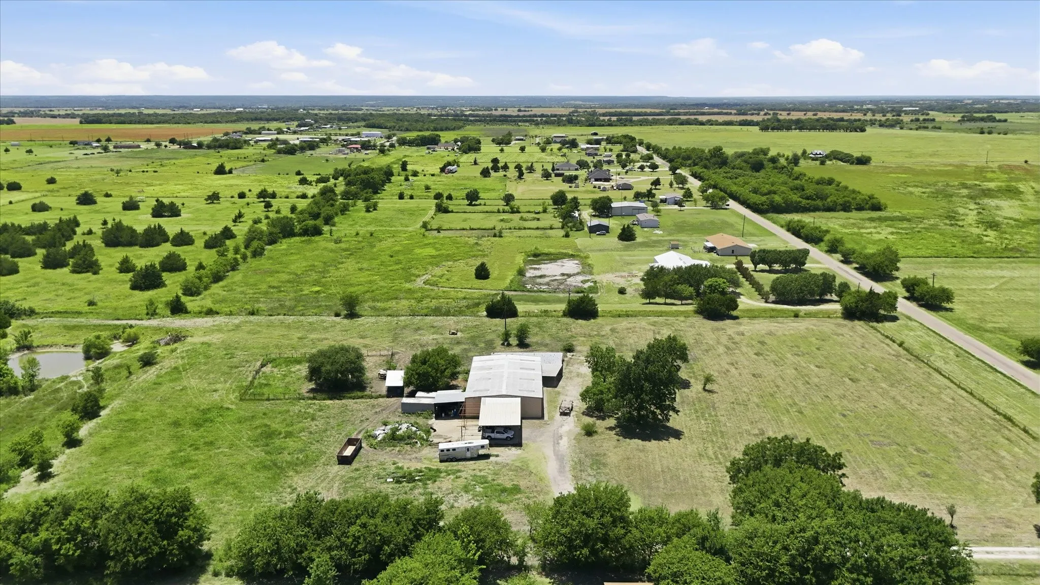 Expansive rural property featuring a primary residence with an attached garage, a large outbuilding, and a gravel driveway