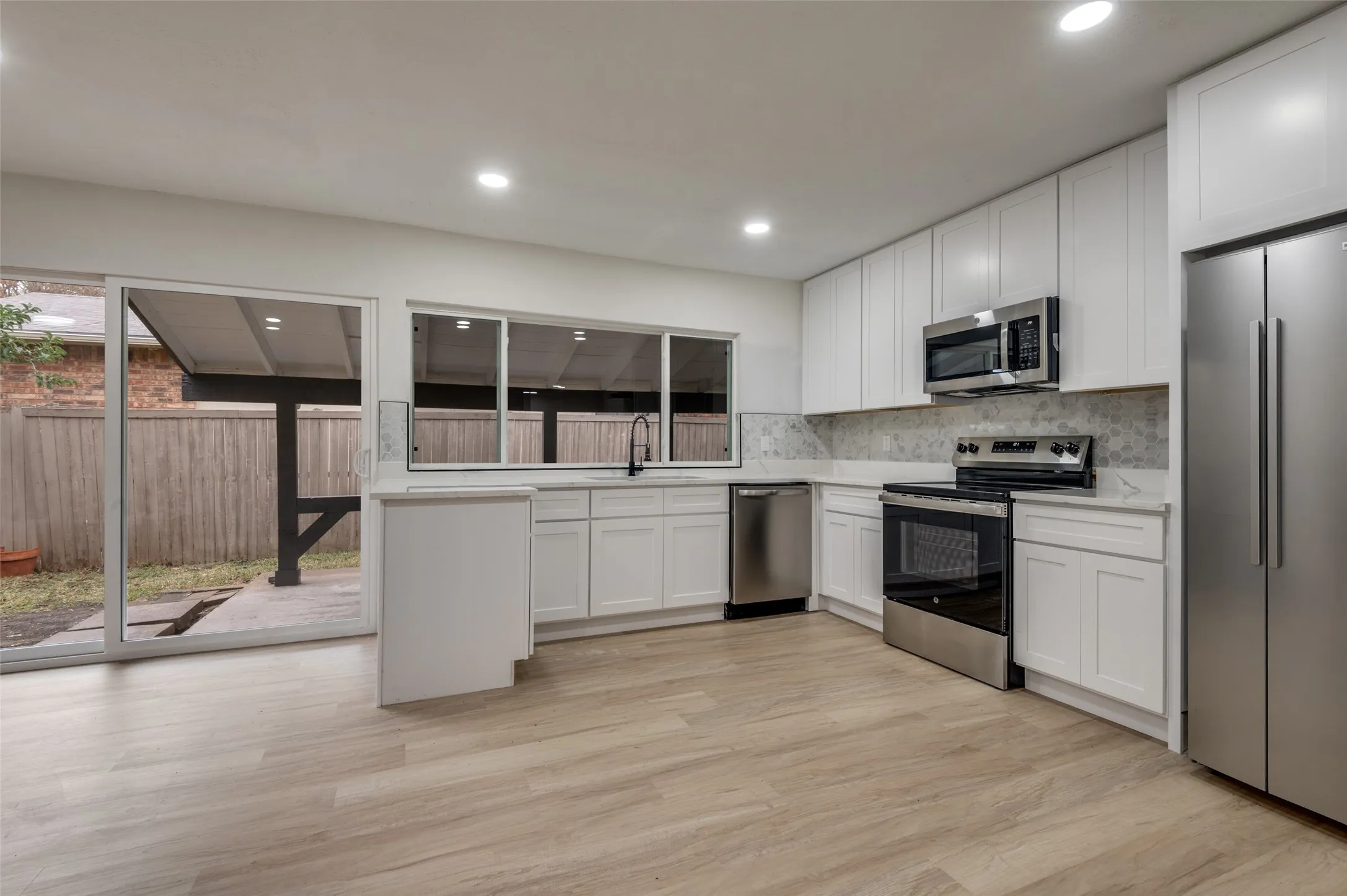 Contemporary kitchen featuring white cabinetry, stainless steel appliances, light-toned wood-finish flooring, a patterned backsplash, and a sliding glass door to the exterior