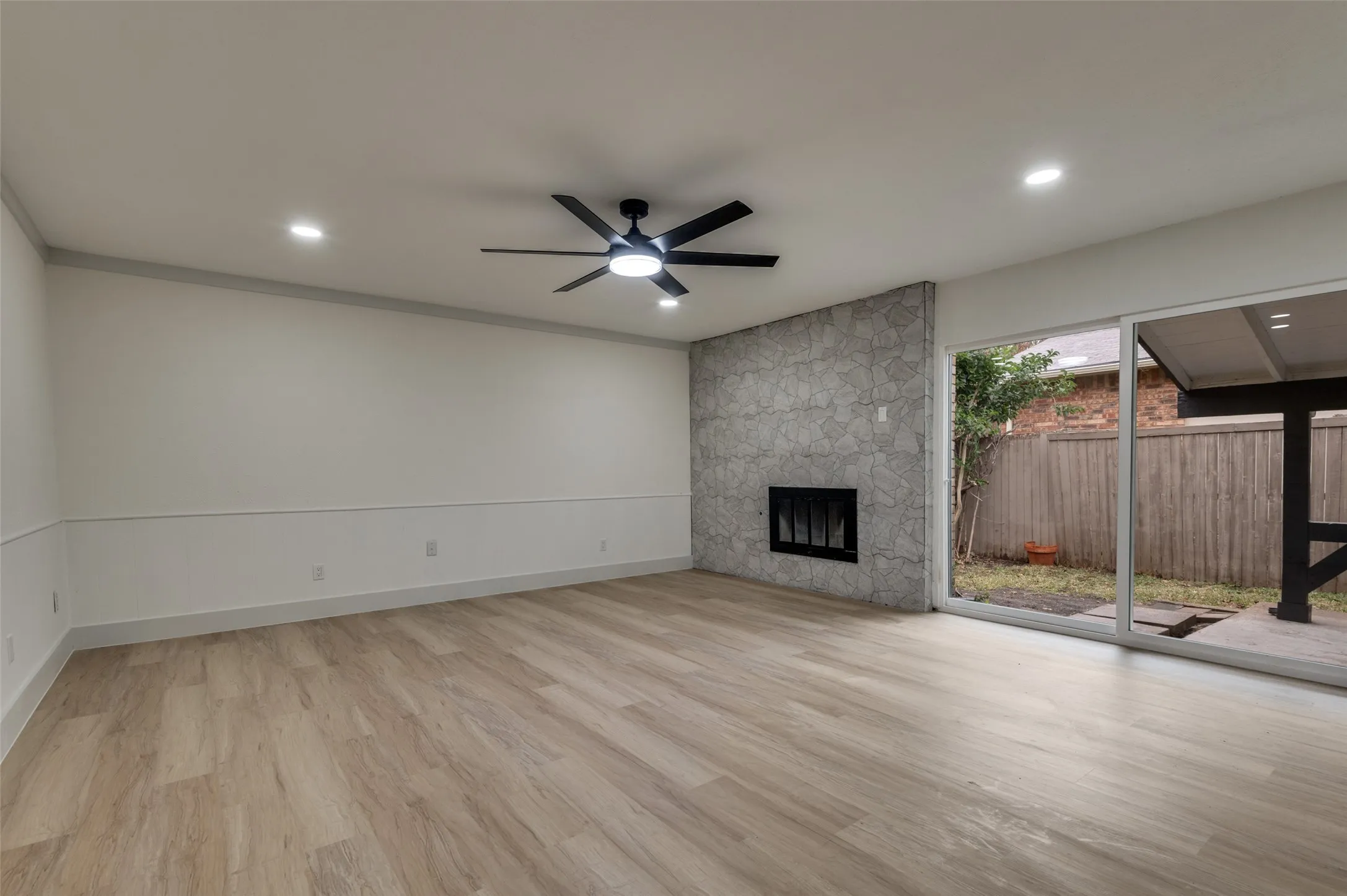 Spacious room featuring wood-finish flooring, a stone-clad fireplace, and sliding glass doors opening to an outdoor area