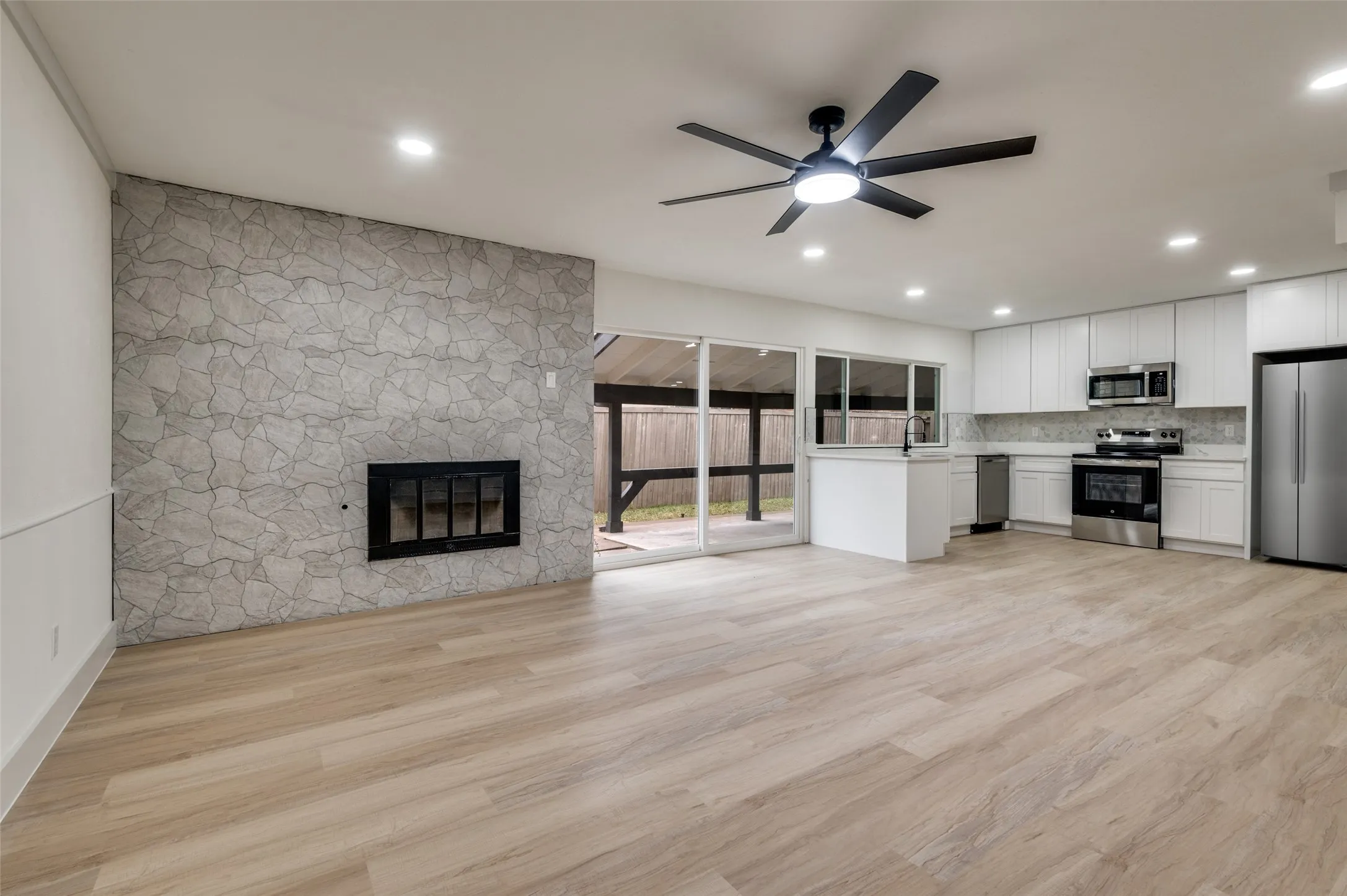 Open-concept living space featuring wood-finish flooring, a stone-clad fireplace, recessed lighting, and a modern ceiling fan