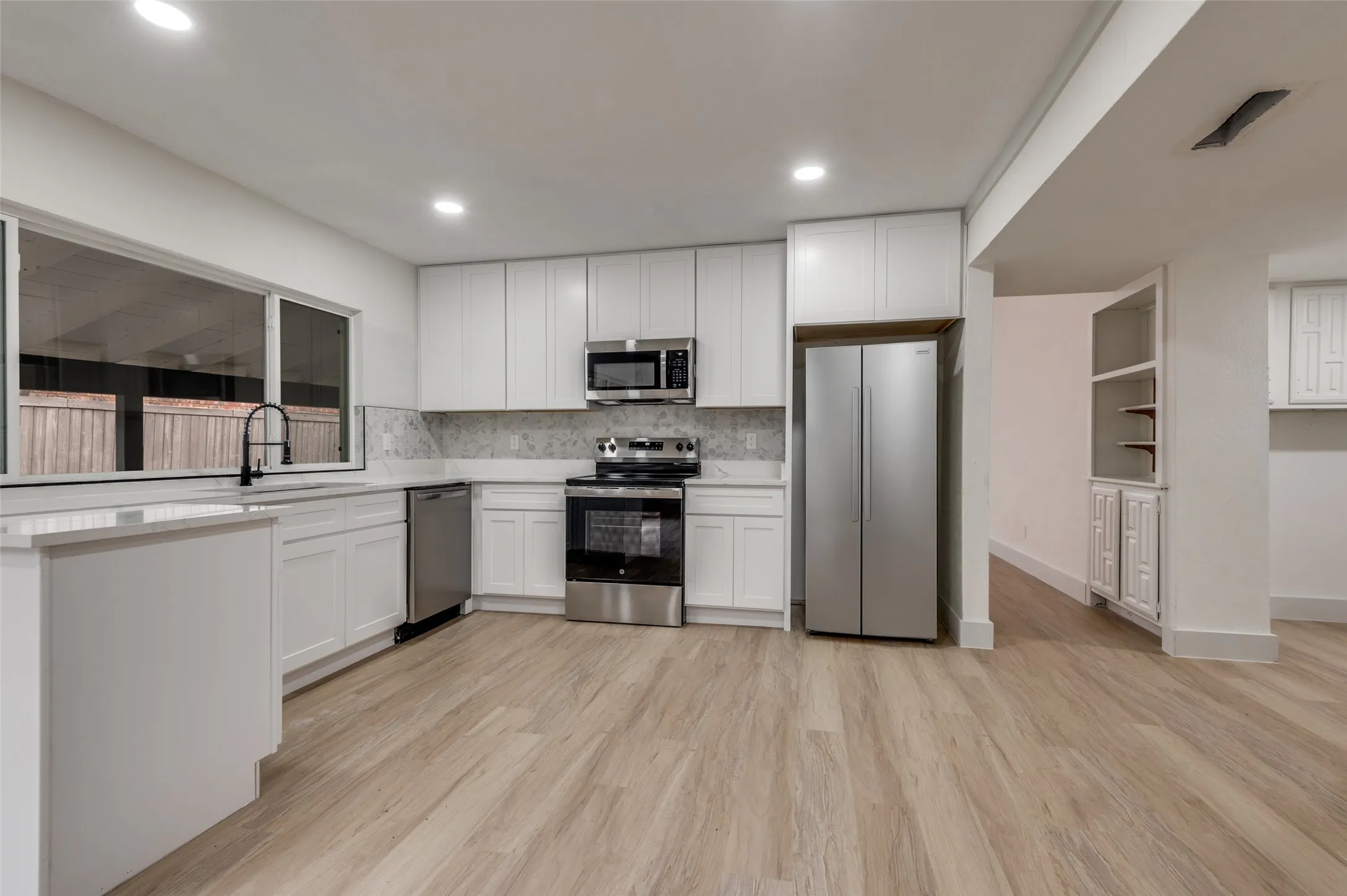 Kitchen featuring white cabinetry, stainless steel appliances, wood-finish flooring, quartz-look countertops, and a full-height tile backsplash