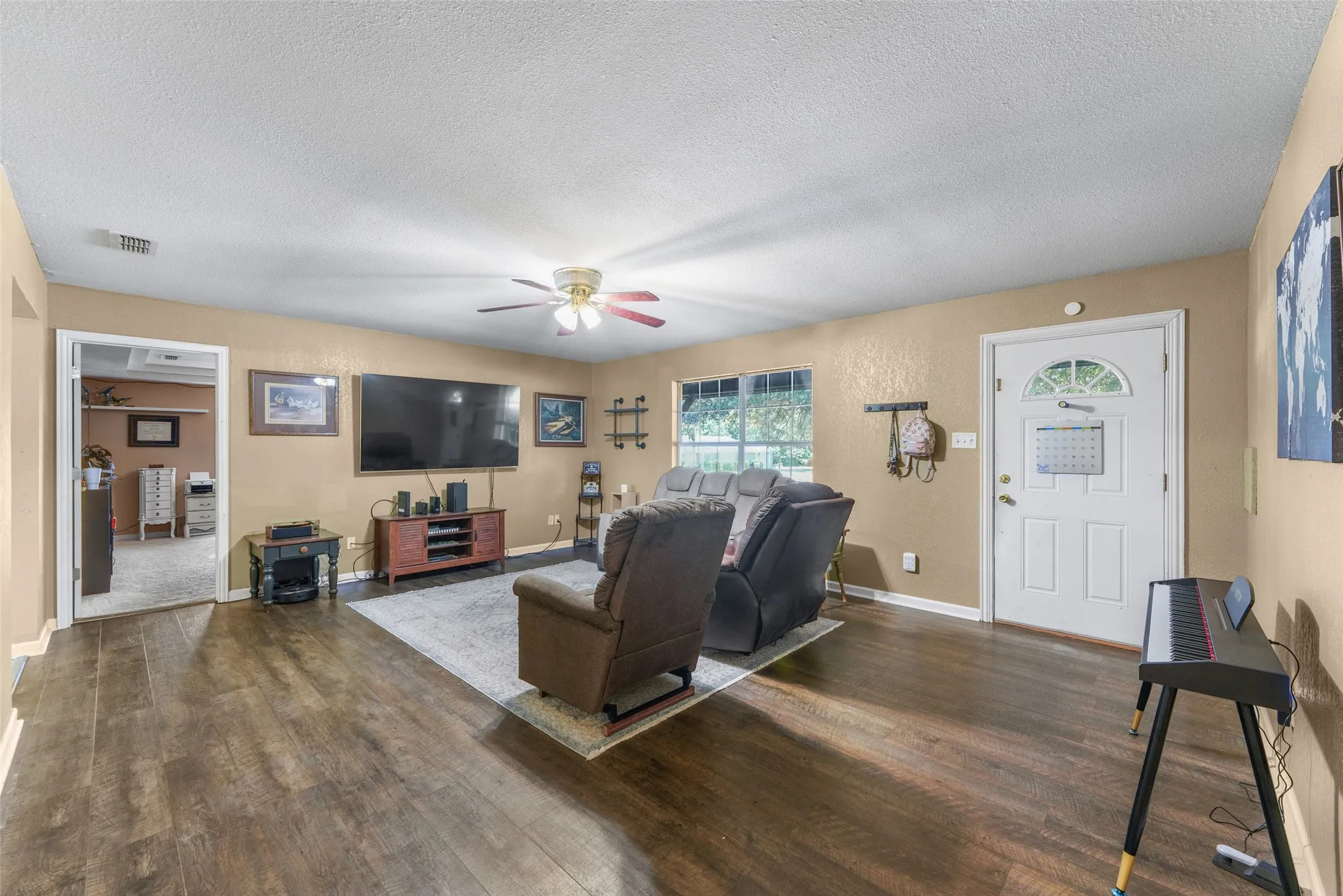 Spacious living area featuring wood-finish flooring, a ceiling fan with integrated lighting, and multiple windows providing natural light