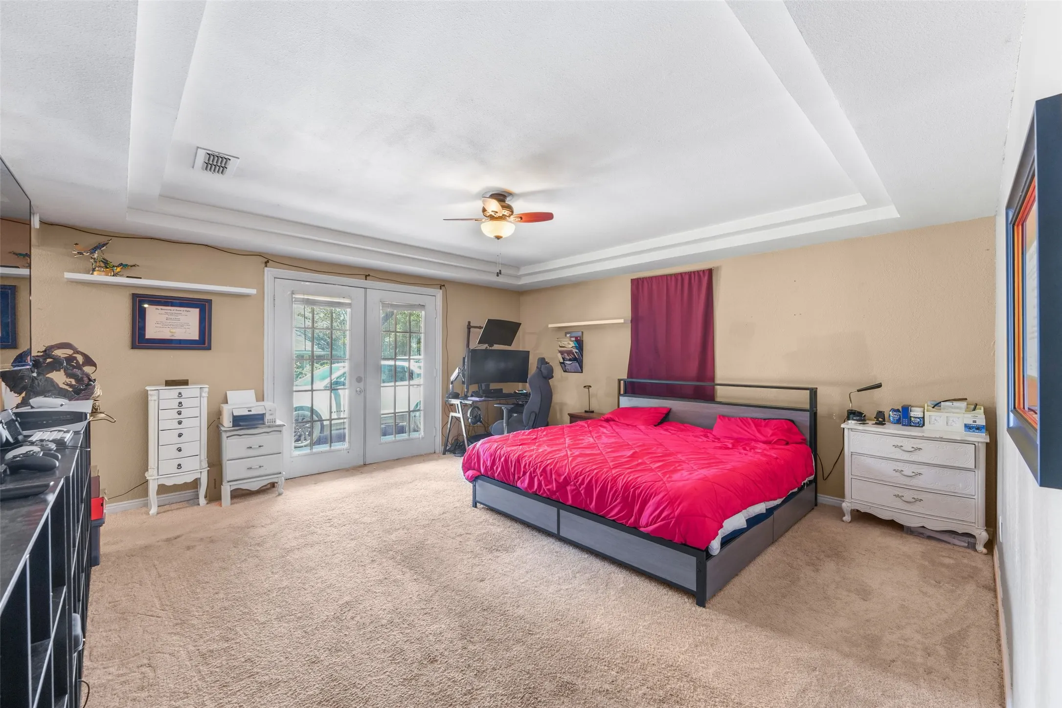 Recessed tray ceiling with crown molding, ceiling fan, and neutral carpet flooring
