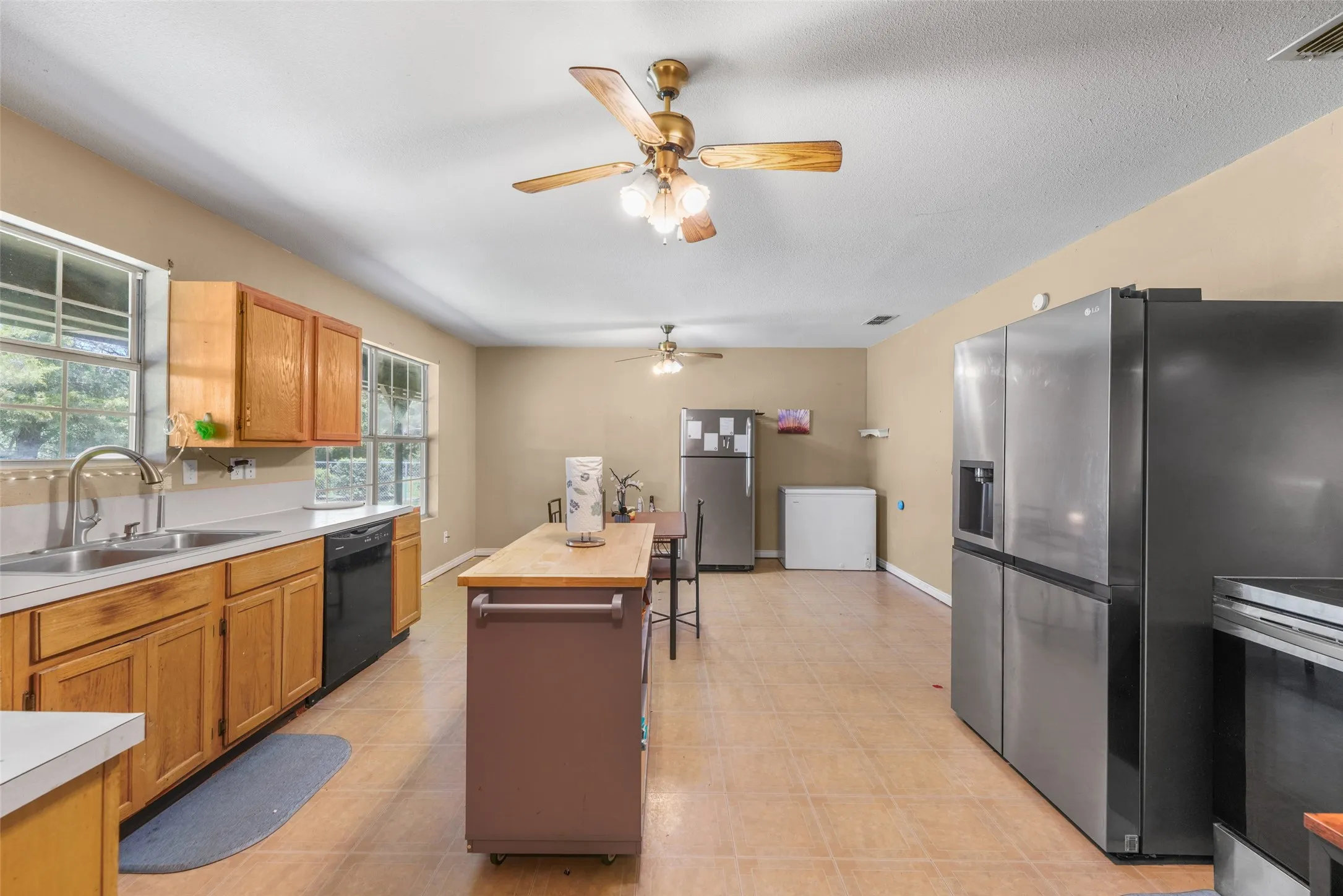 Open-concept kitchen featuring wood cabinetry, white countertops, dual basin sink with gooseneck faucet, black dishwasher, and tile flooring